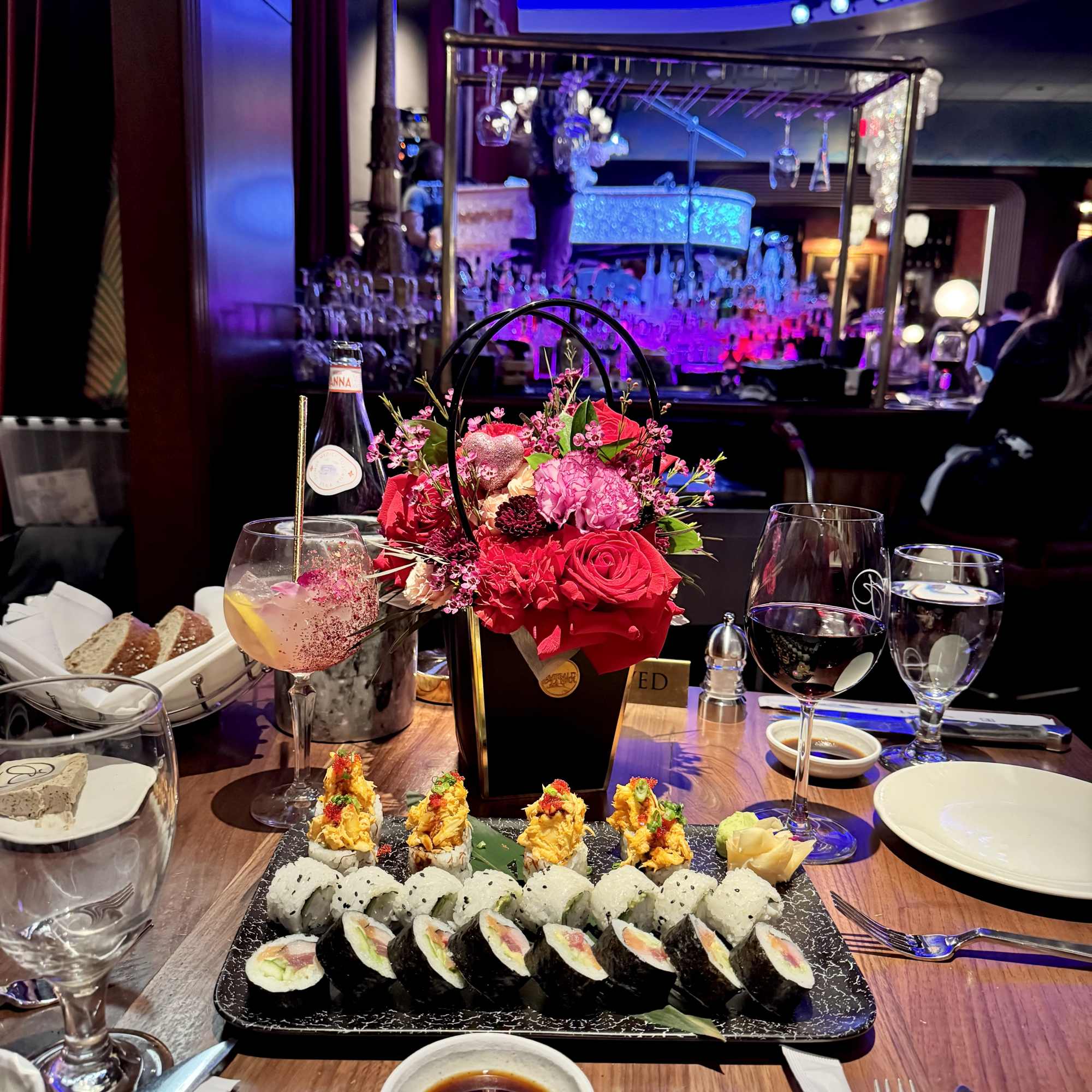 Red and pink floral centerpiece on a restaurant table with sushi and wine glasses