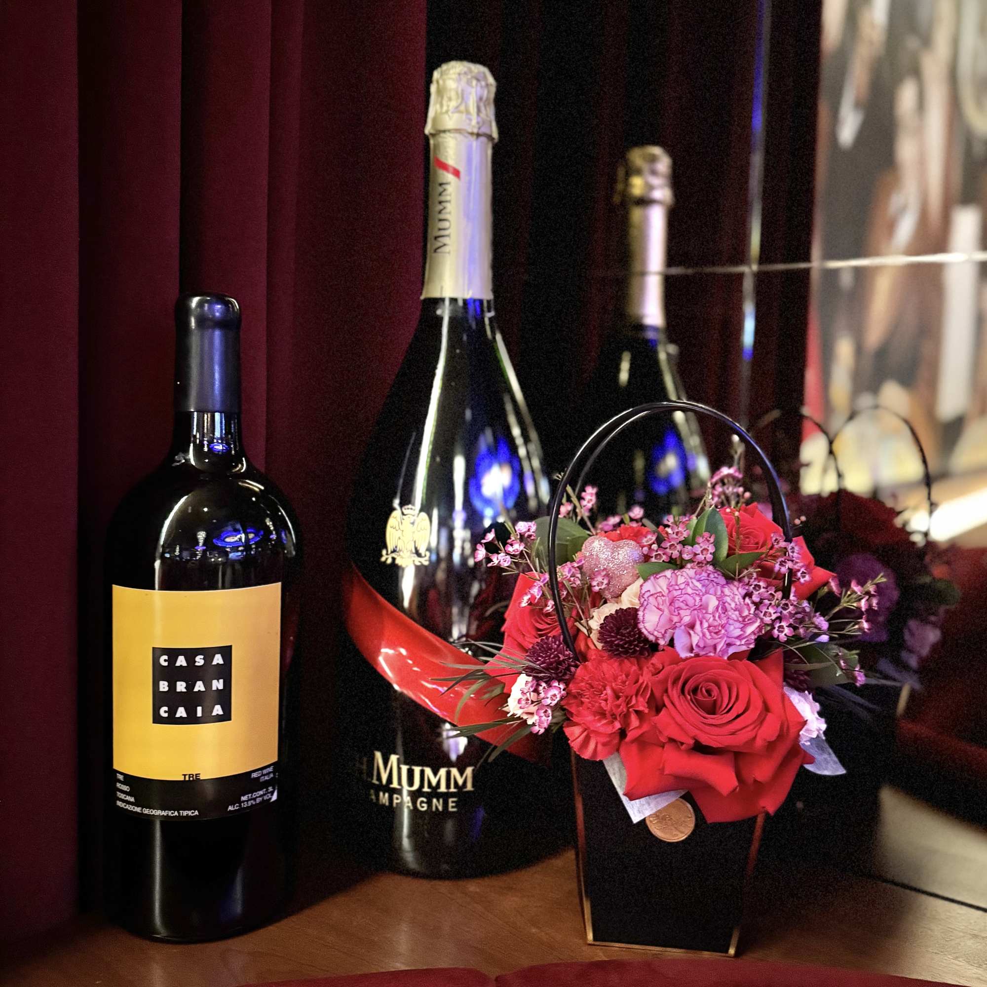 Flower basket with red and pink roses beside wine and champagne bottles