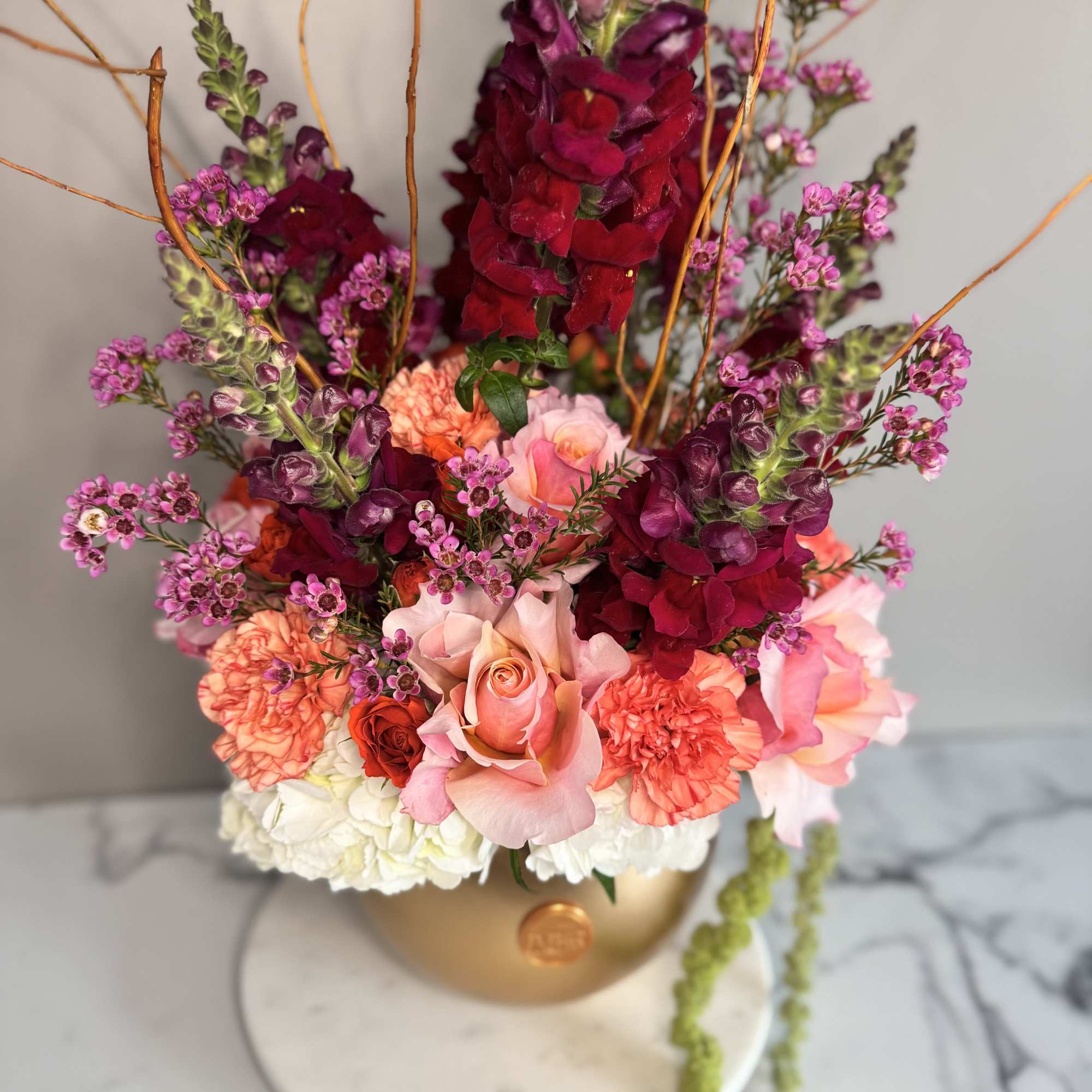 Mixed bouquet in a gold vase with pink, coral, and burgundy flowers