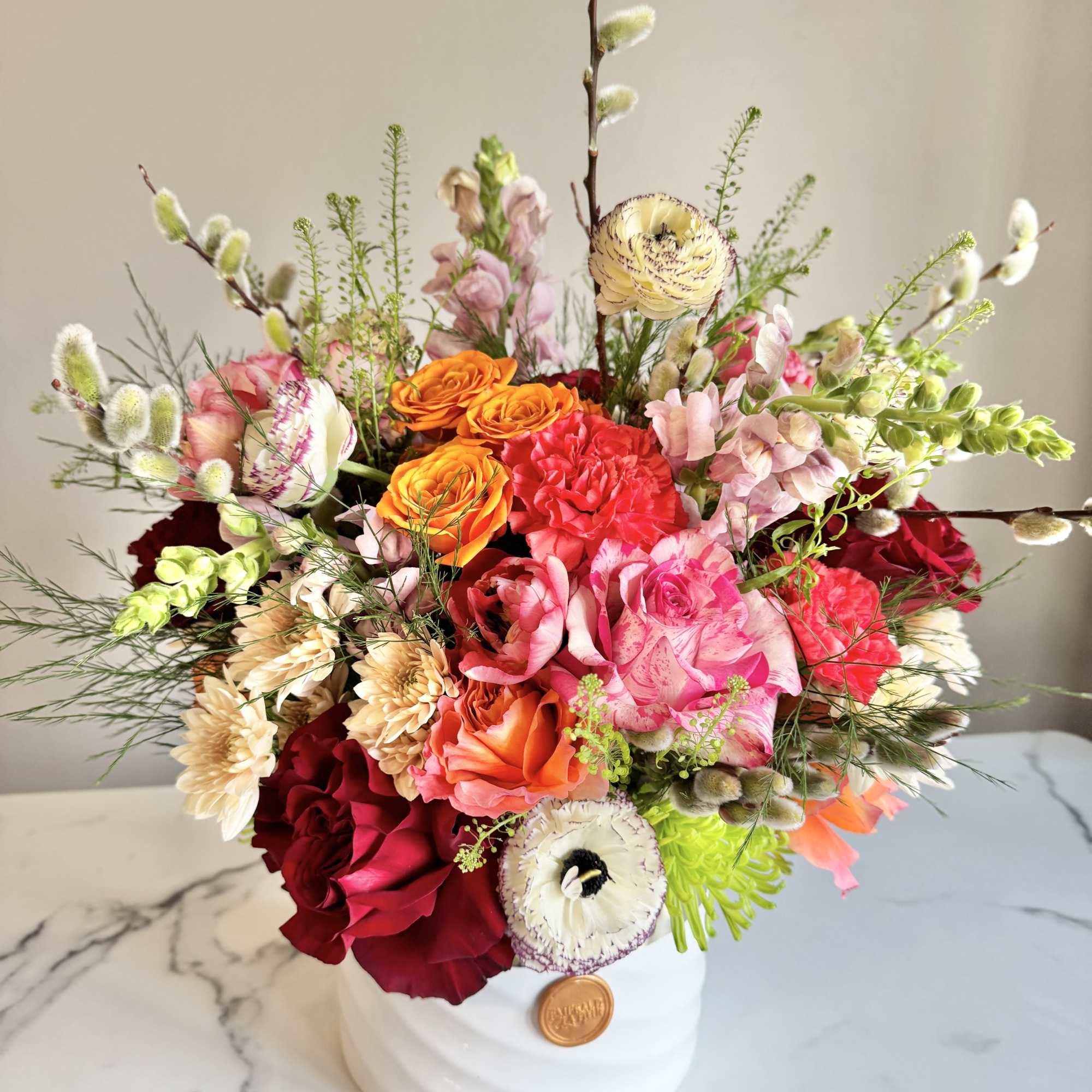 Colorful arrangement of pink, red, and orange flowers in a white ceramic vase on a marble surface