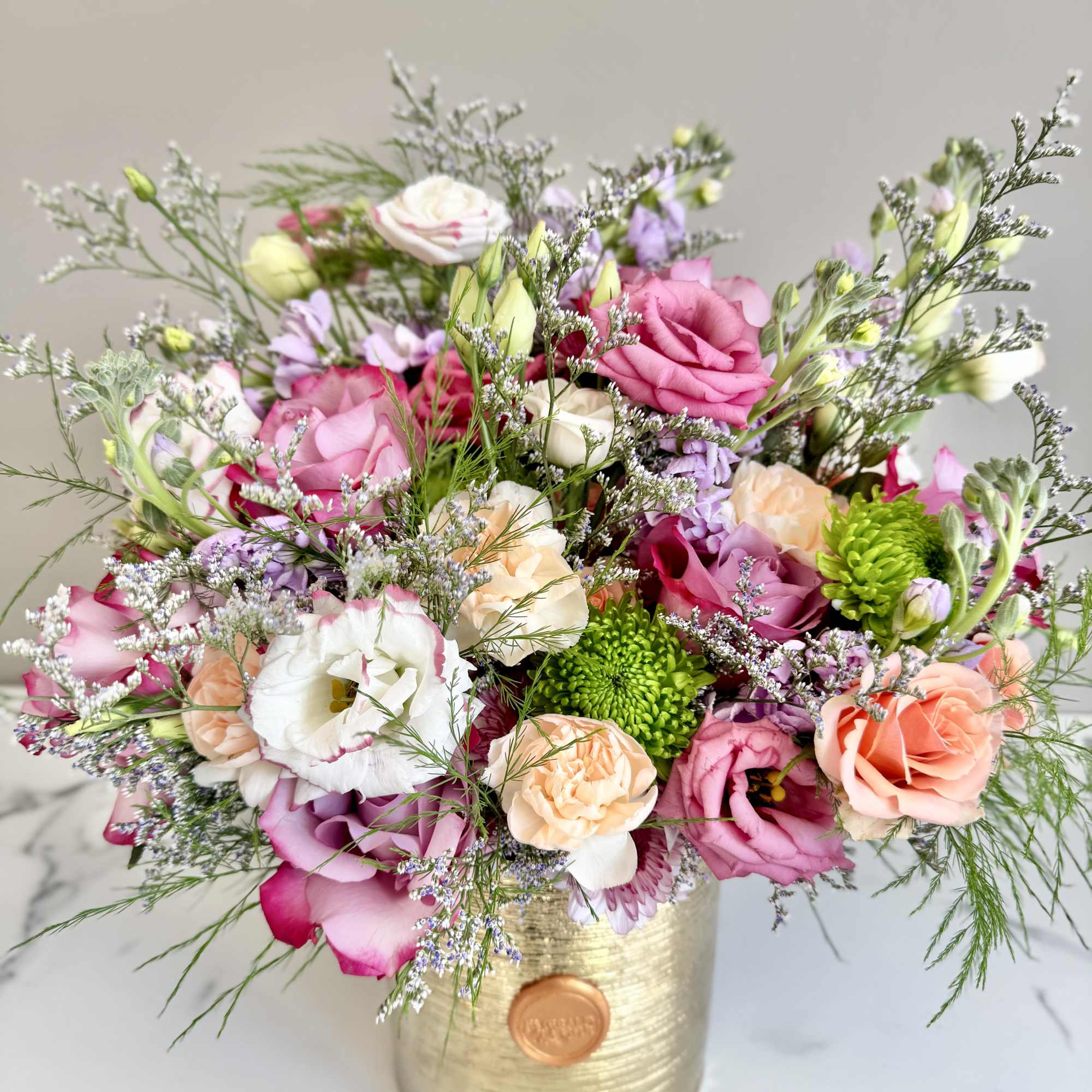 Mixed bouquet of pink and peach roses and white lisianthus in a gold cylinder vase