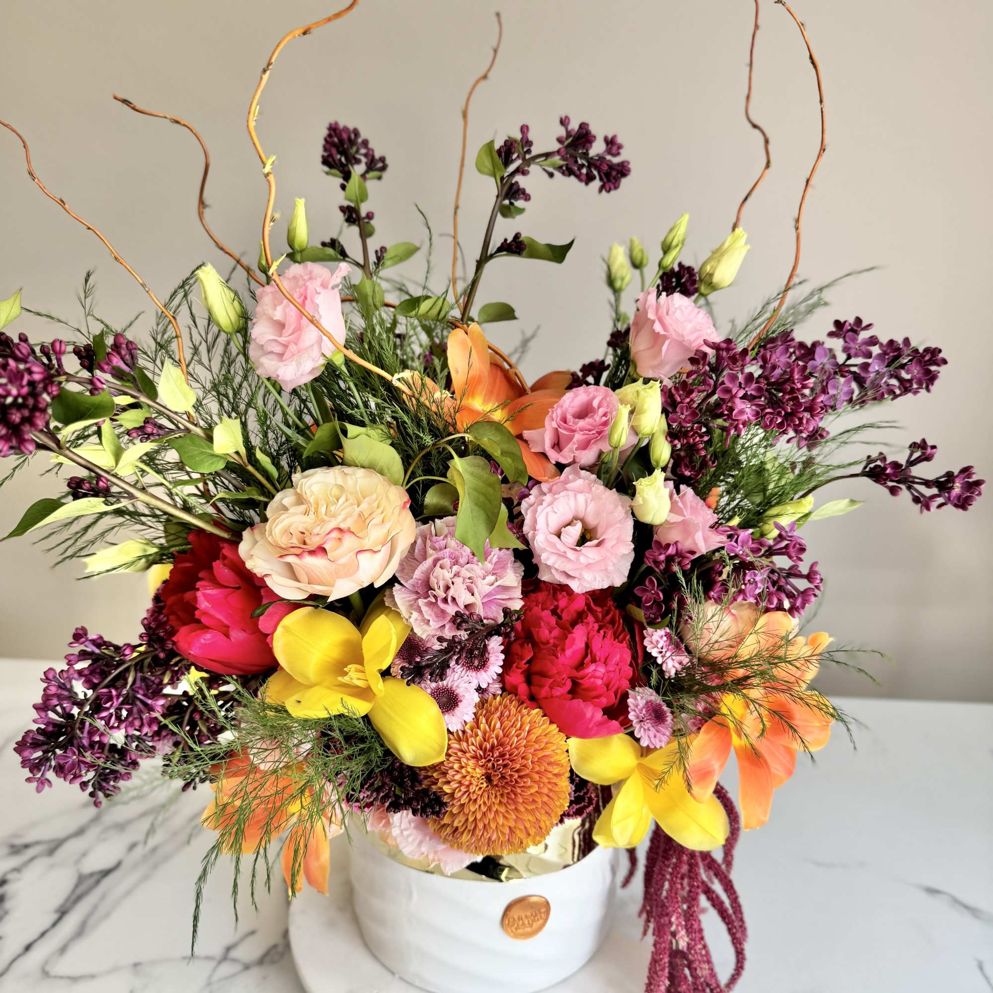Colorful arrangement of pink lisianthus, peonies, lilies, and yellow tulips in a white round vase