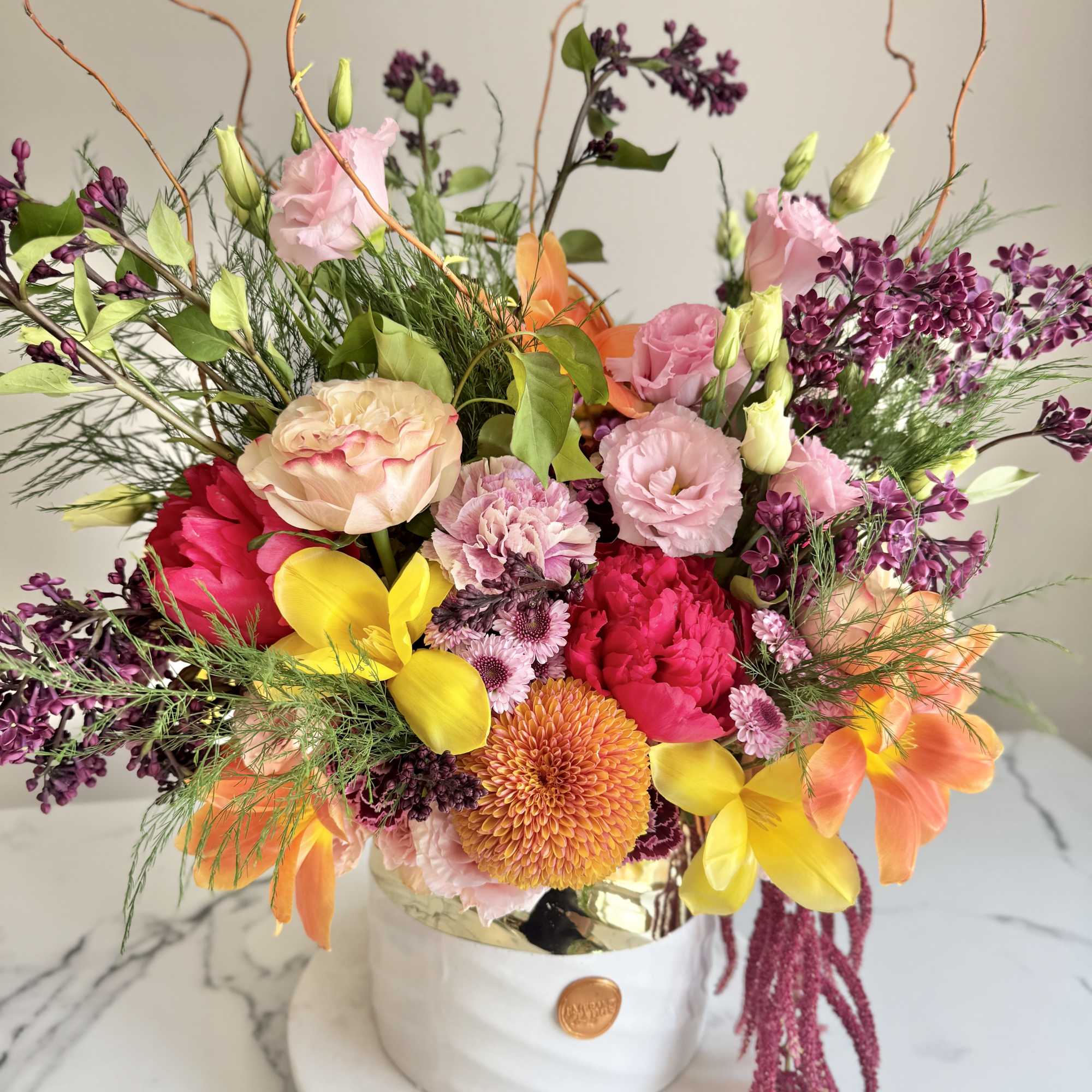 Colorful arrangement of pink, yellow, orange and purple flowers in a white ceramic pot on marble.