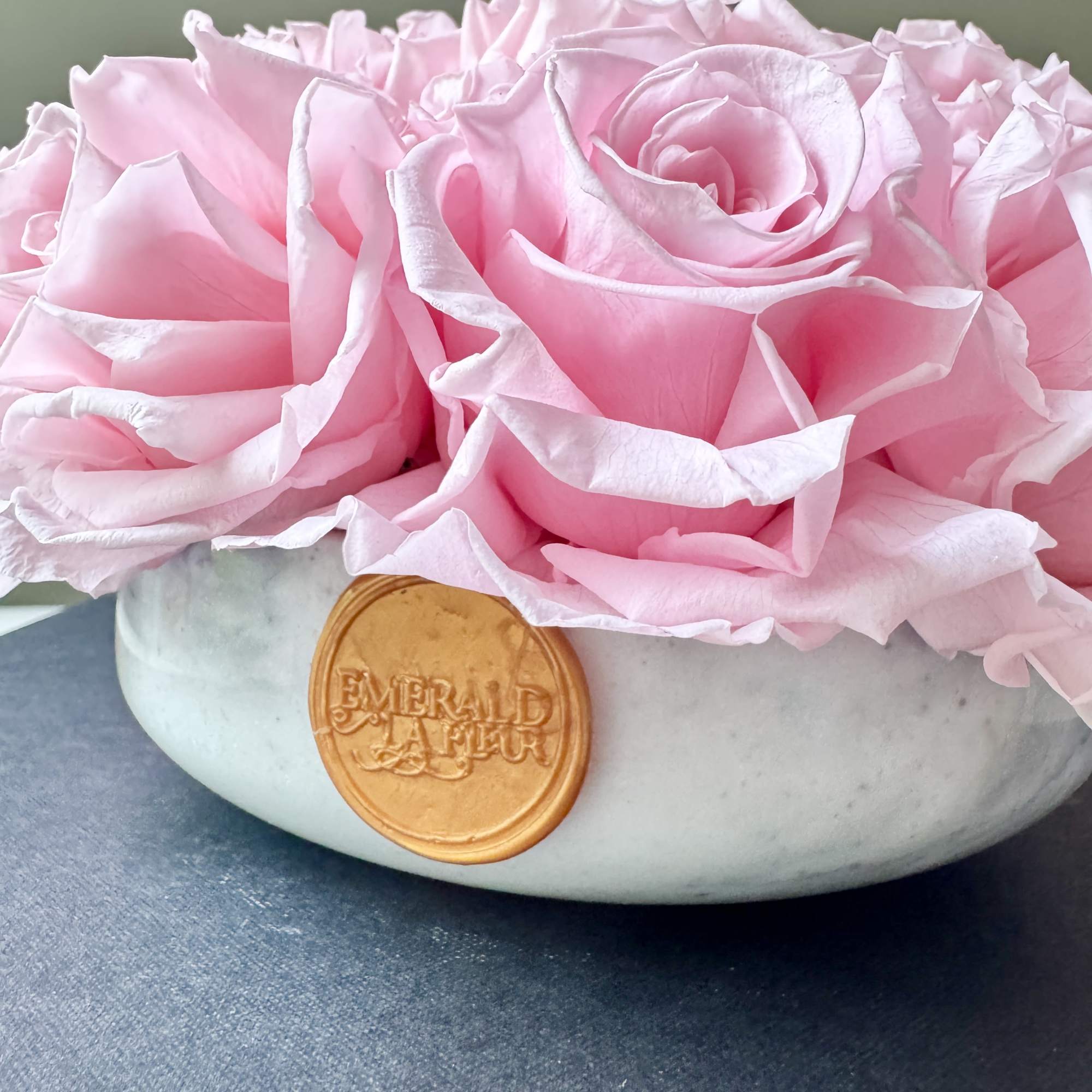 Pink roses arranged in a low white bowl with a gold emblem