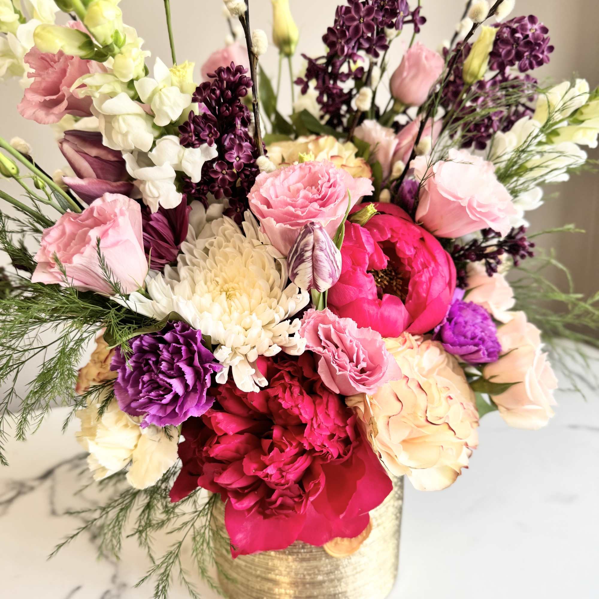 Colorful arrangement of pink peonies, roses, and mixed blooms in a gold vase