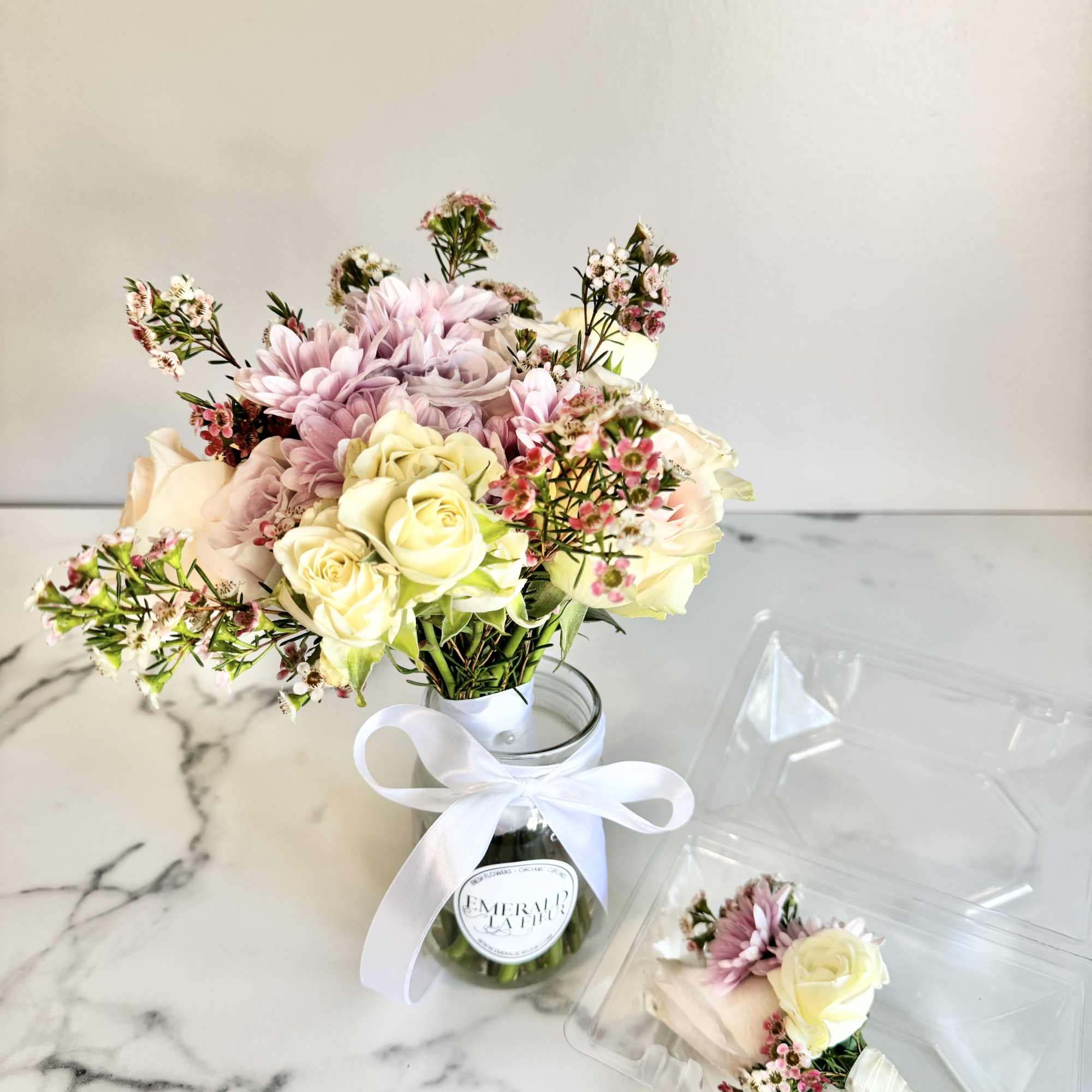Bouquet of pale roses and pink daisies in a glass jar with a white ribbon