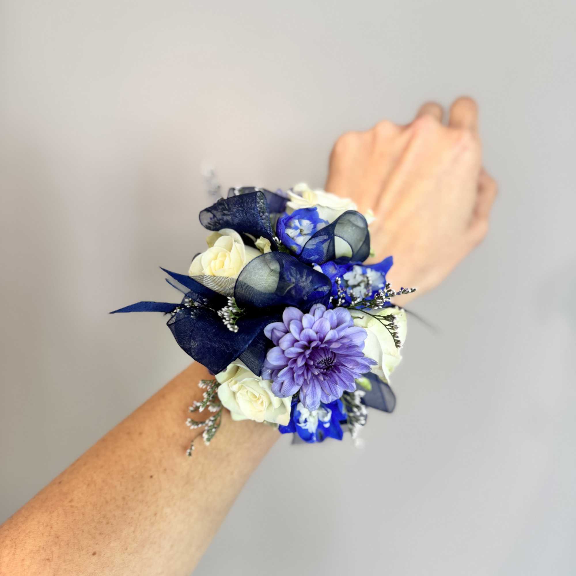 Wrist corsage with white and purple flowers and navy ribbon