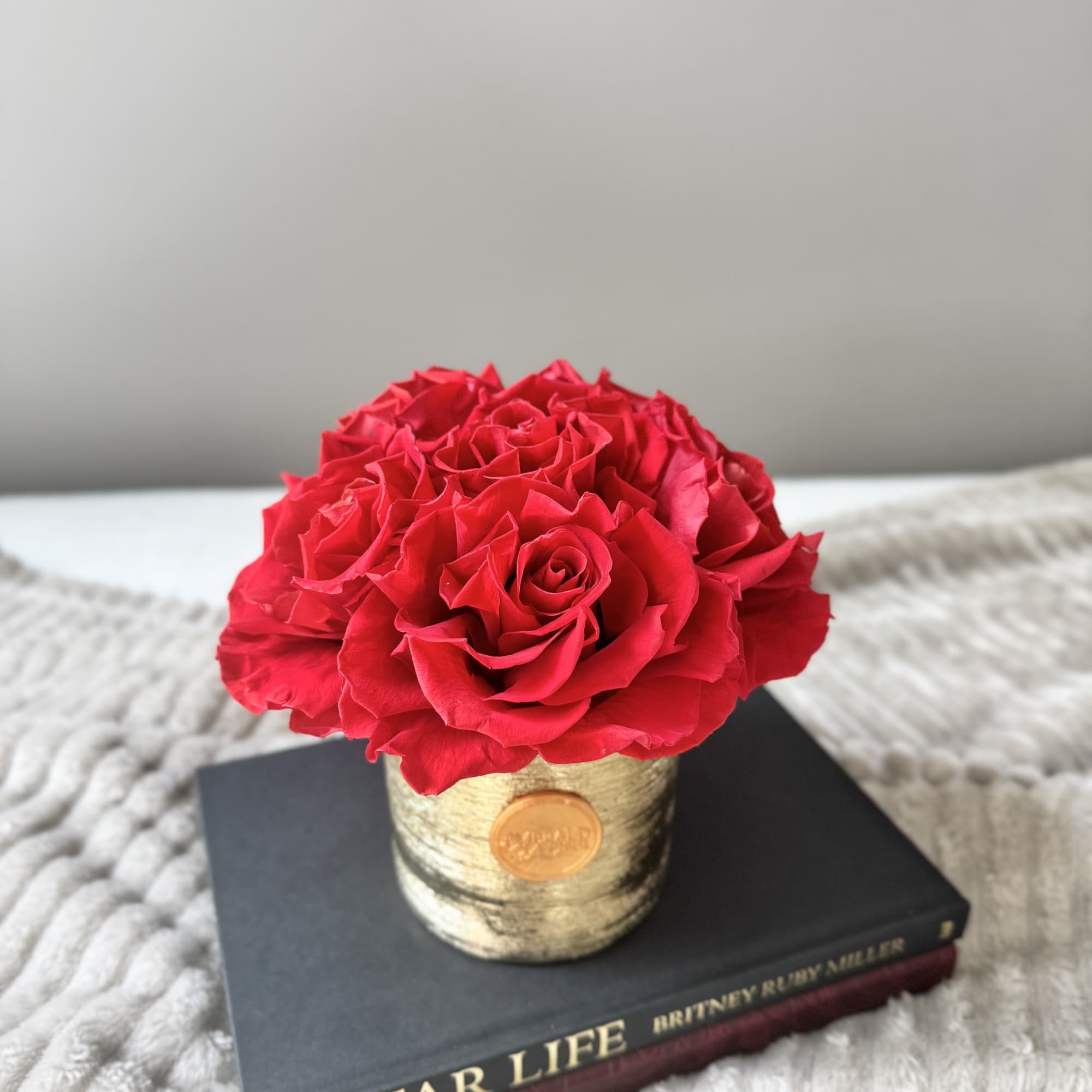 Red rose bouquet in a gold-toned container on a book