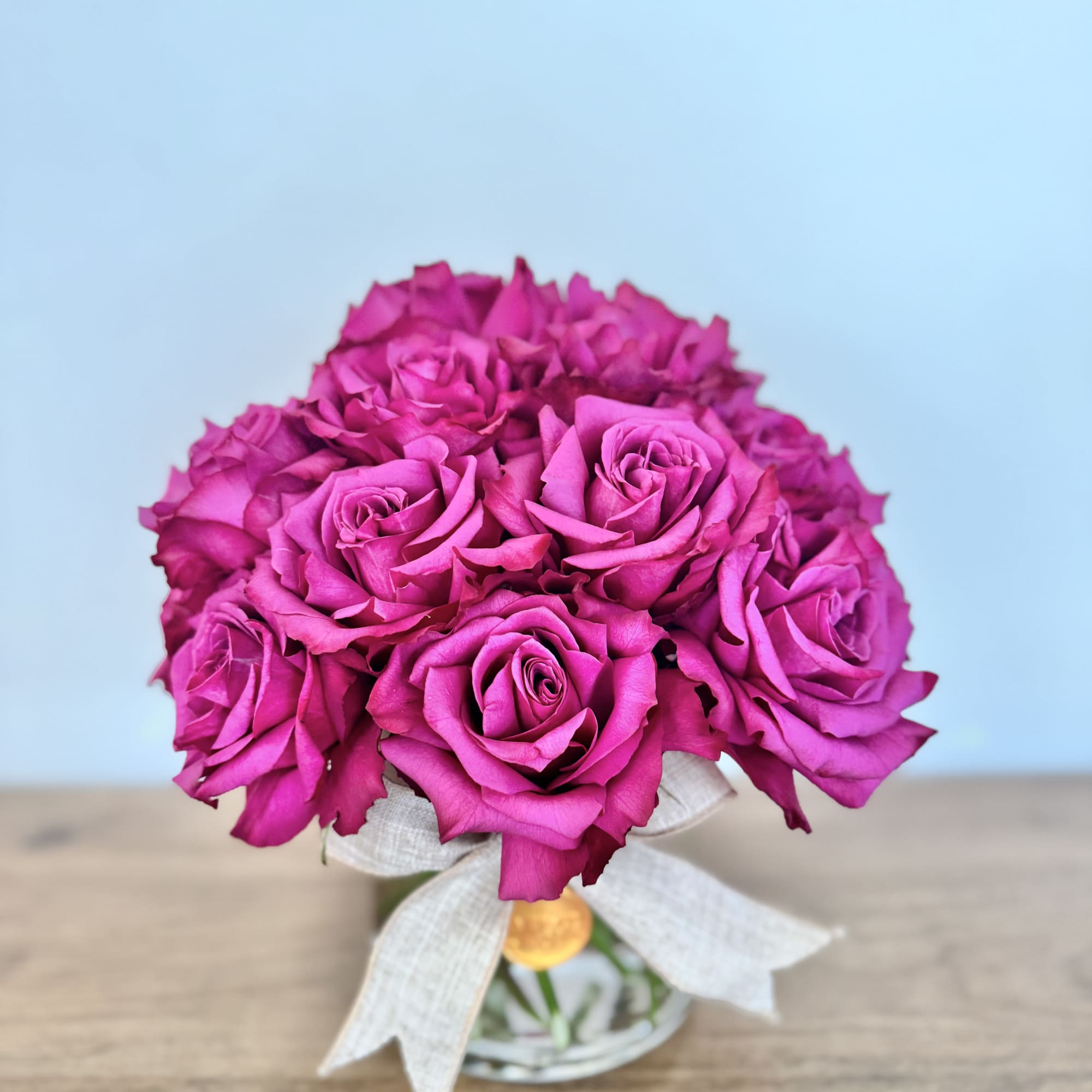 Bouquet of bright pink roses in a small glass vase with a white ribbon