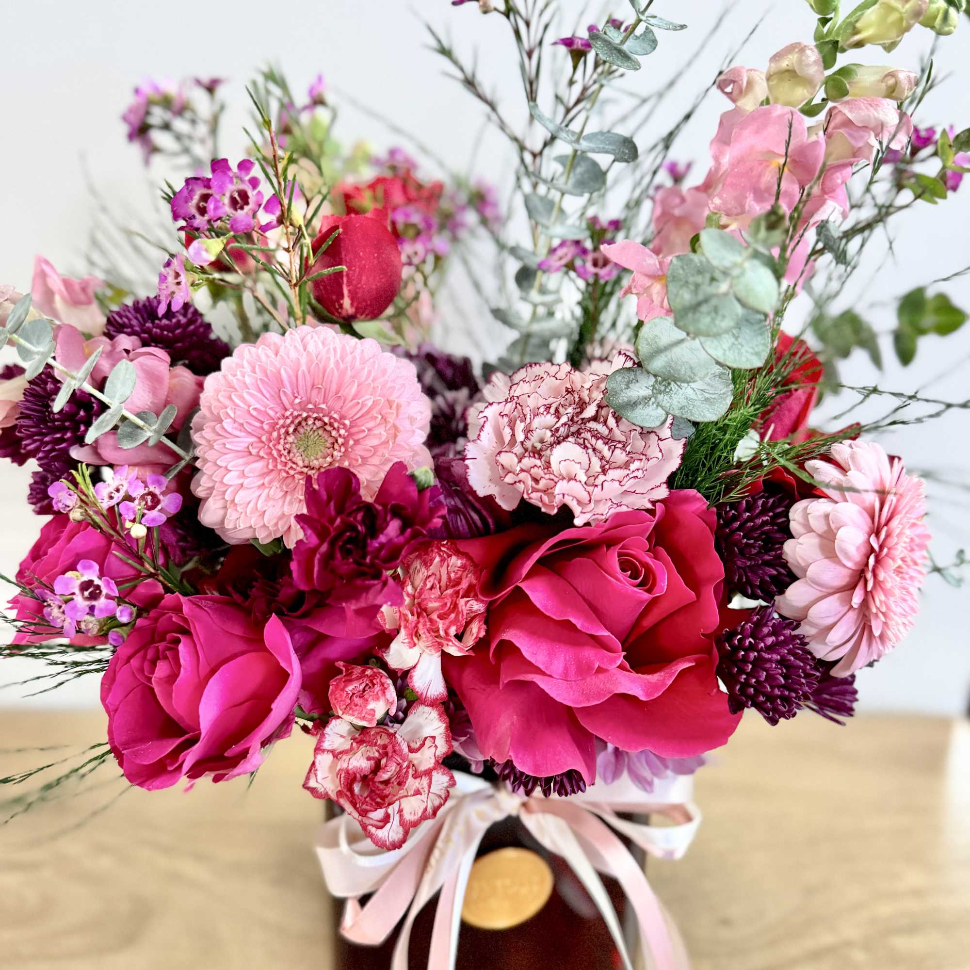 Pink and magenta flower arrangement in a dark vase with ribbon