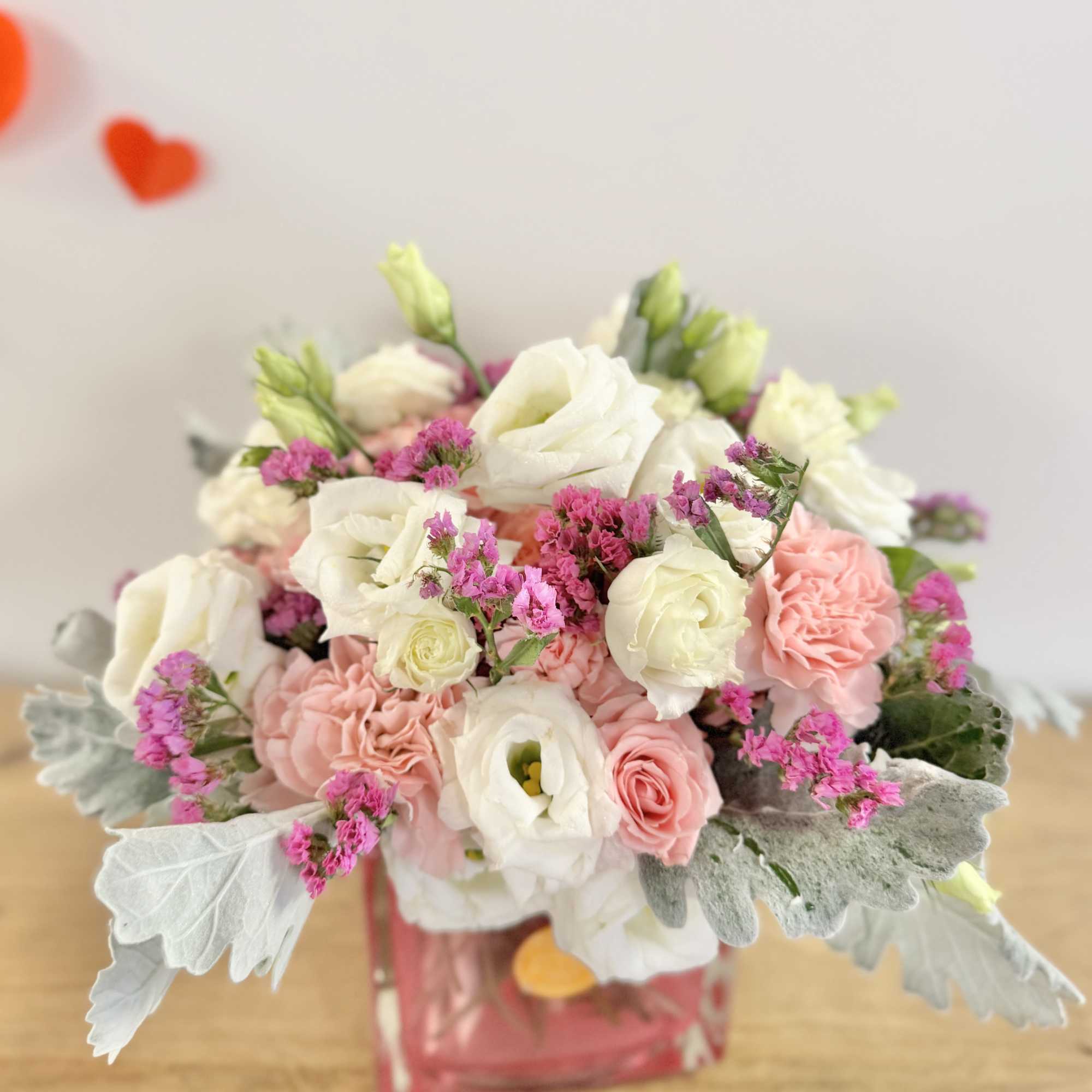 Compact pink and white bouquet with lisianthus and roses in a pink glass cube vase with silvery foliage.