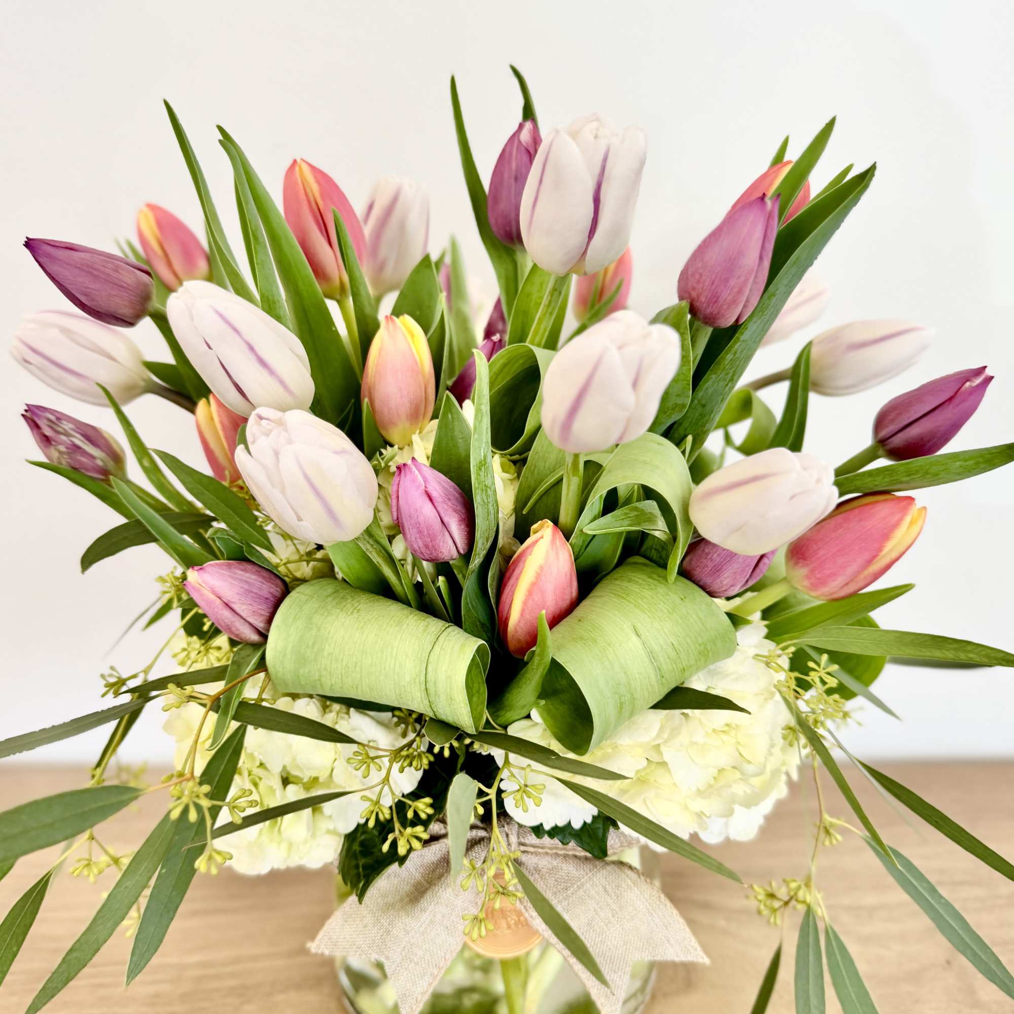 Pink and white tulips arranged in a glass vase with a burlap bow