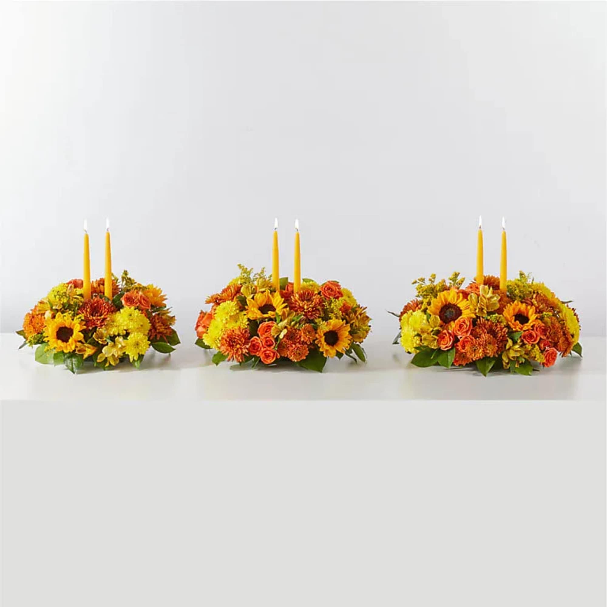 Three low floral centerpieces with yellow candles and orange blooms