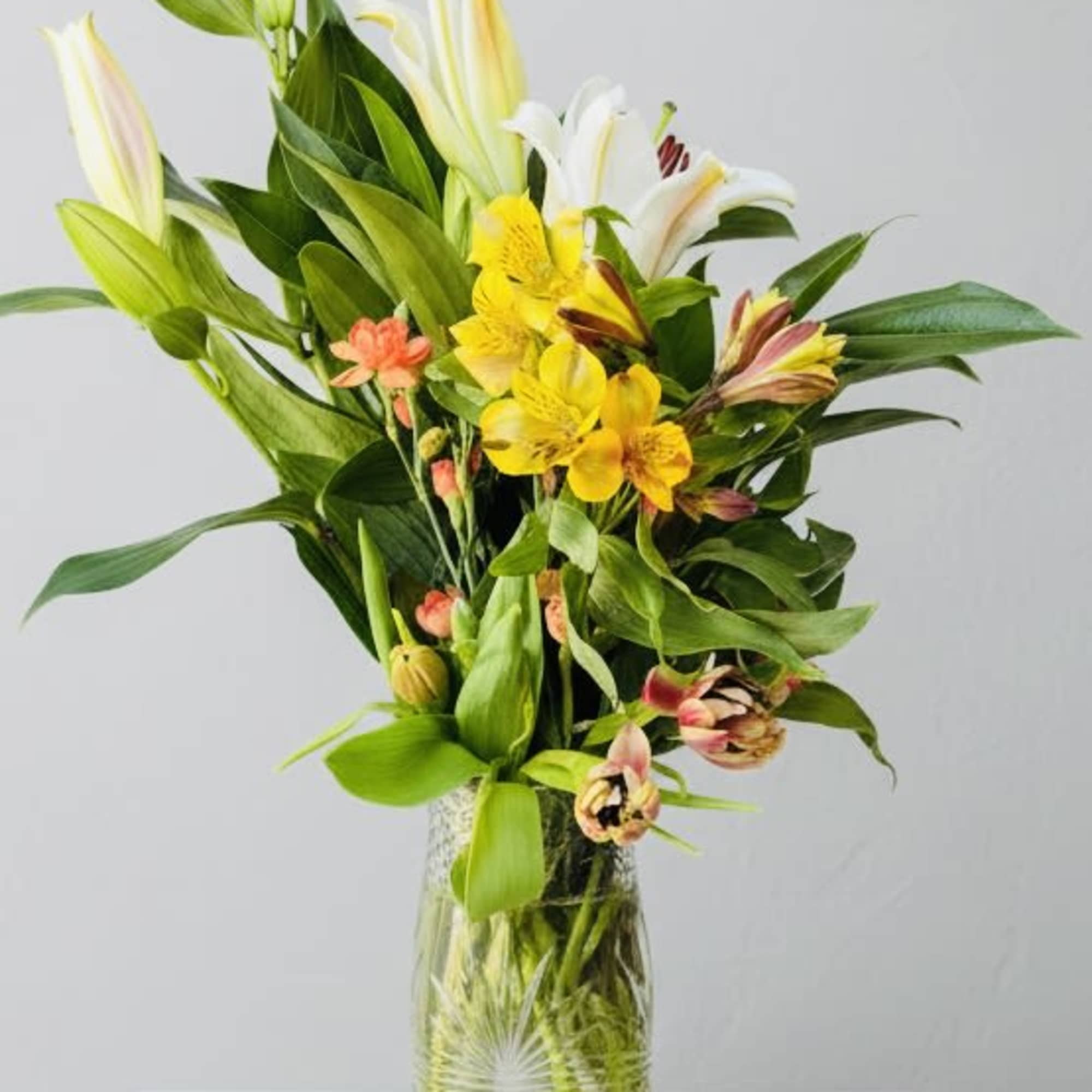 Tall white lilies rise above cheerful yellow alstroemerias with soft pink accents