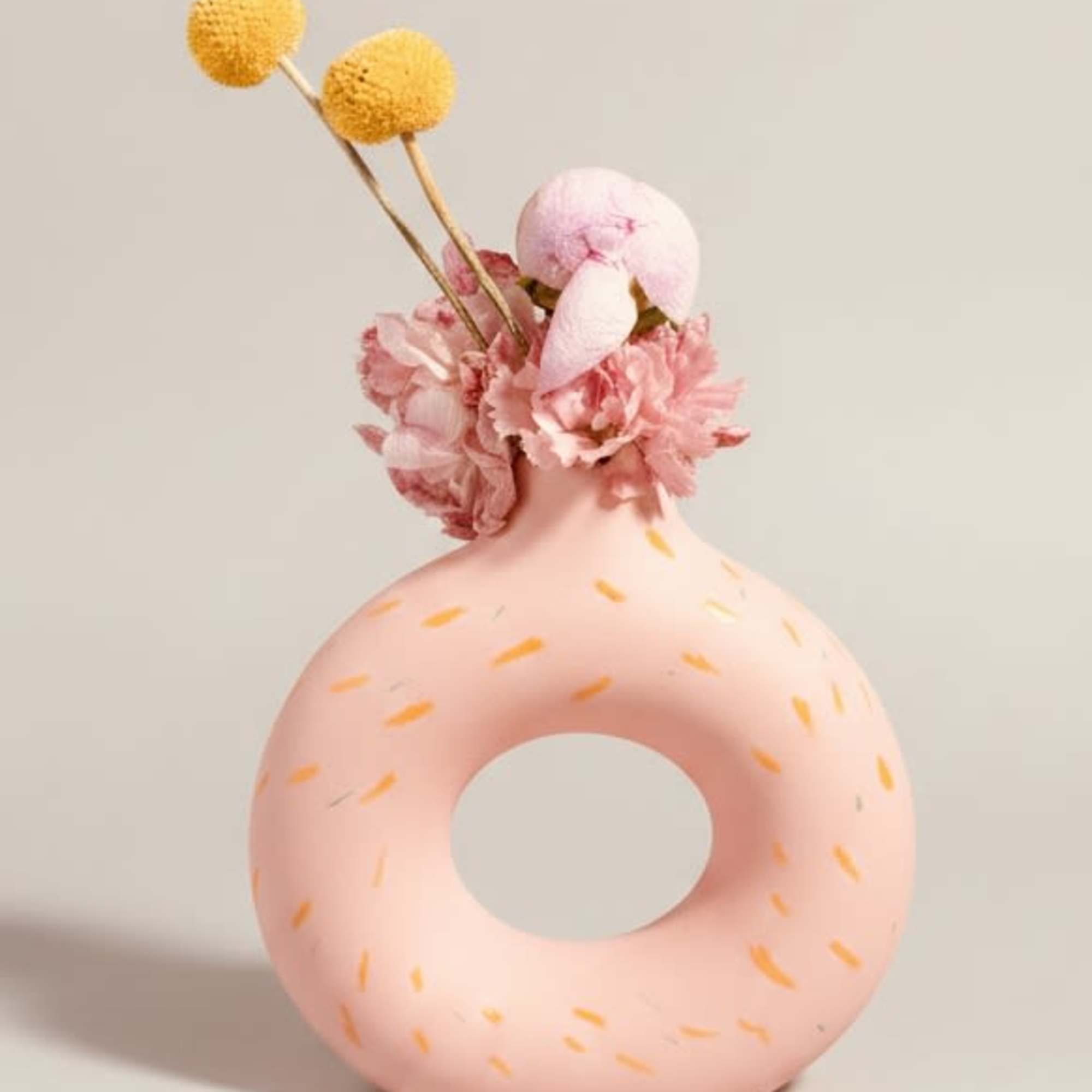 A pastel pink donut-shaped ceramic vase with orange speckled accents makes a