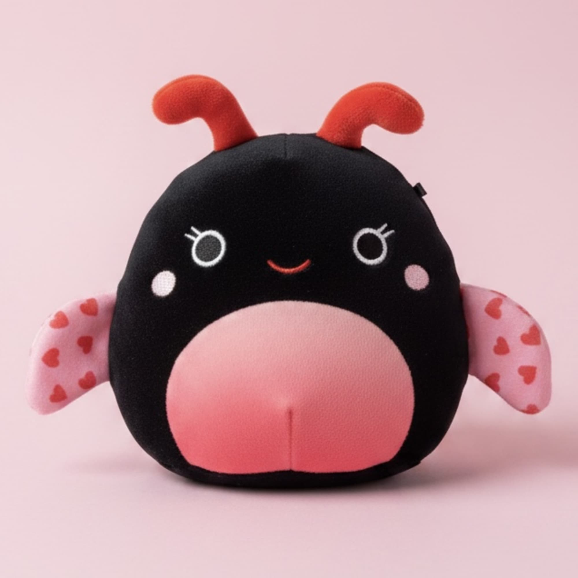 Plush ladybug toy with pink wings on a pink background