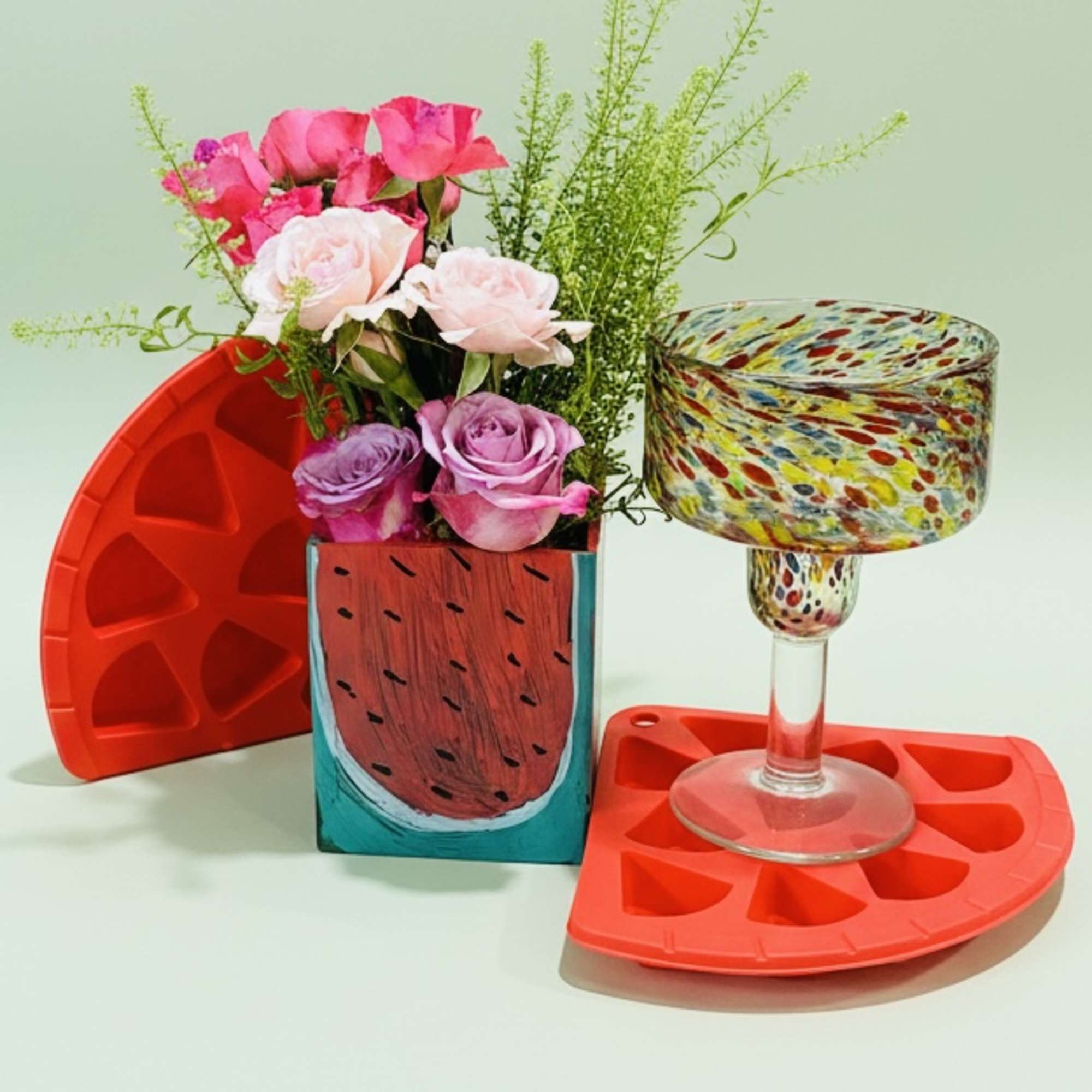 Pink and lavender roses in a painted square vase with a patterned glass and red trays