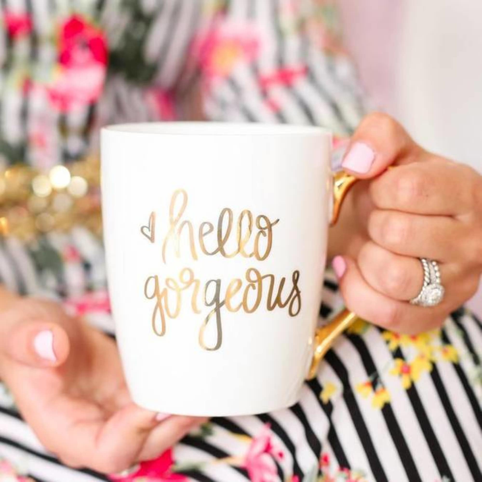 White mug with gold "hello gorgeous" text held in two hands