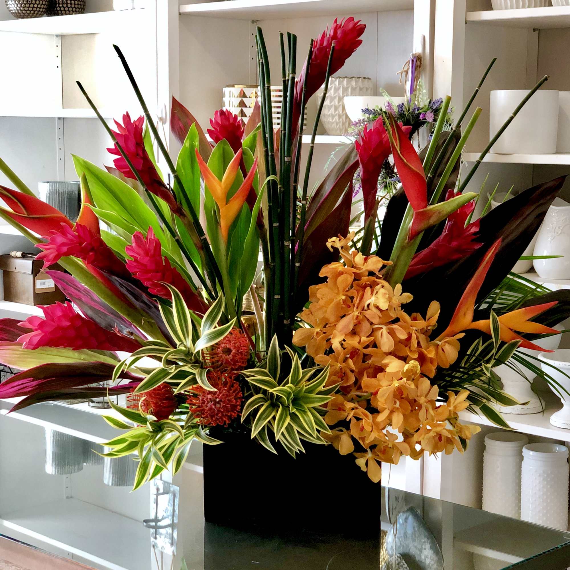 Tropical flower arrangement with red, orange, and yellow blooms in a black container