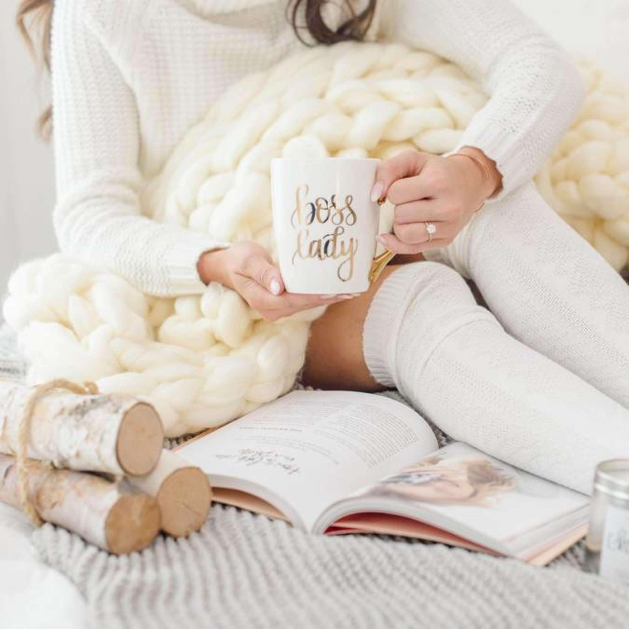 Woman holding a "boss lady" mug while sitting with a chunky knit blanket