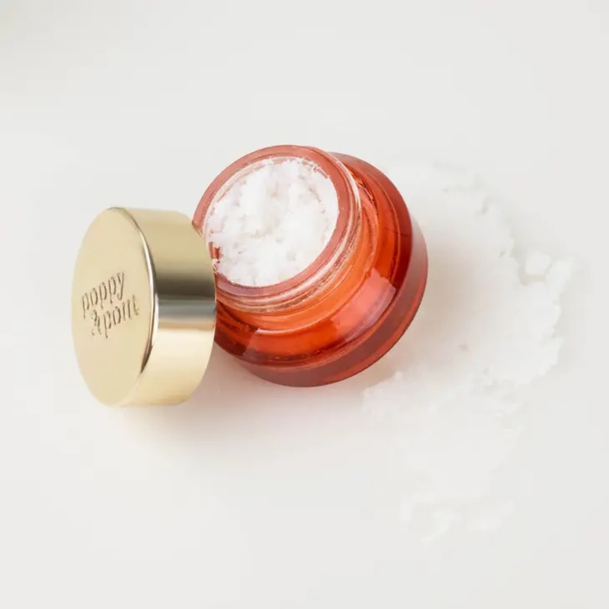Open coral cosmetic jar with gold lid on a white surface