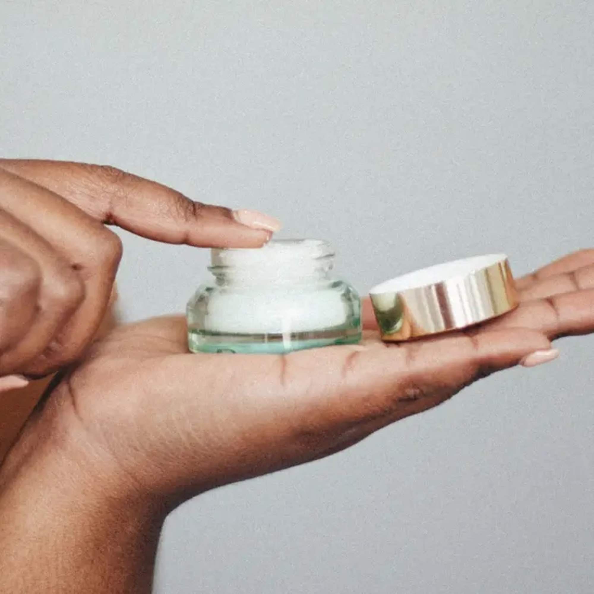 Hands holding a small cream jar and its gold lid