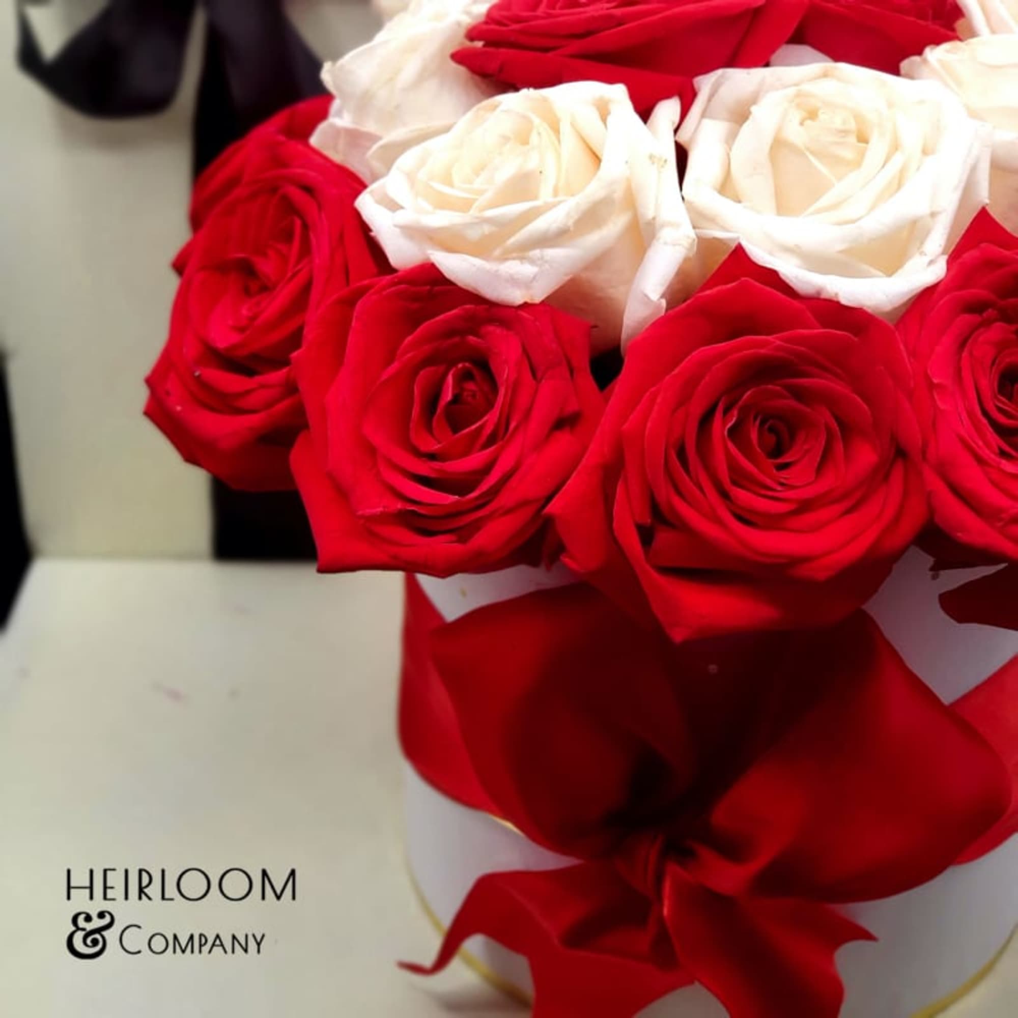 Red and white roses arranged in a white hat box with a red ribbon