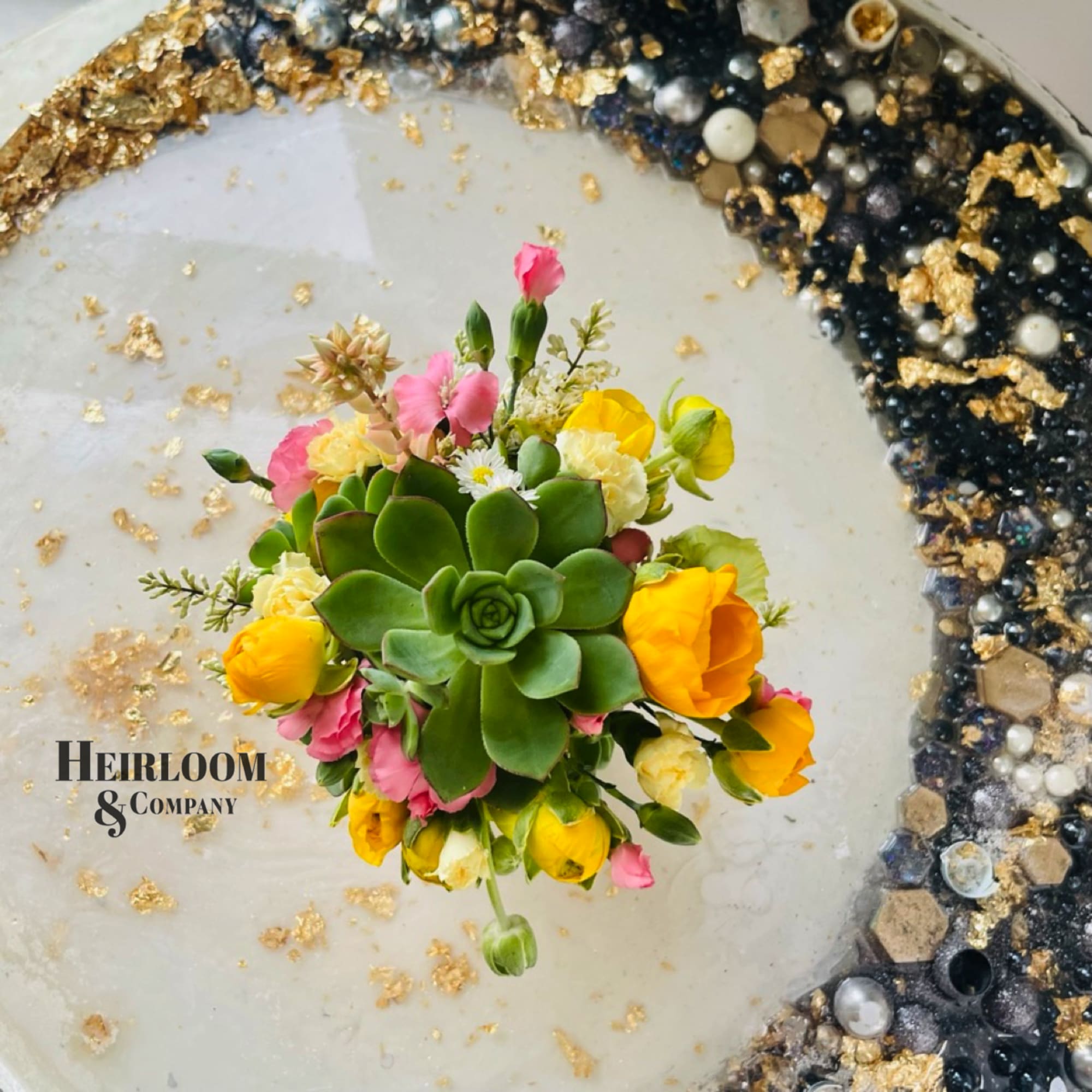 Round floral arrangement with a central succulent and yellow and pink blooms