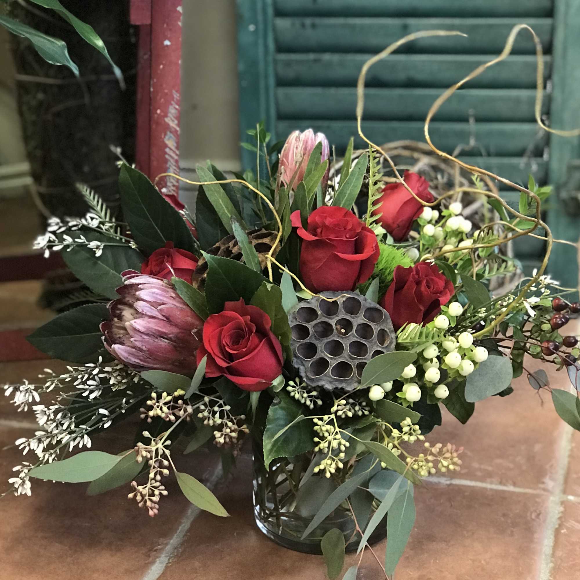 Red roses and pink protea in a glass vase with greenery