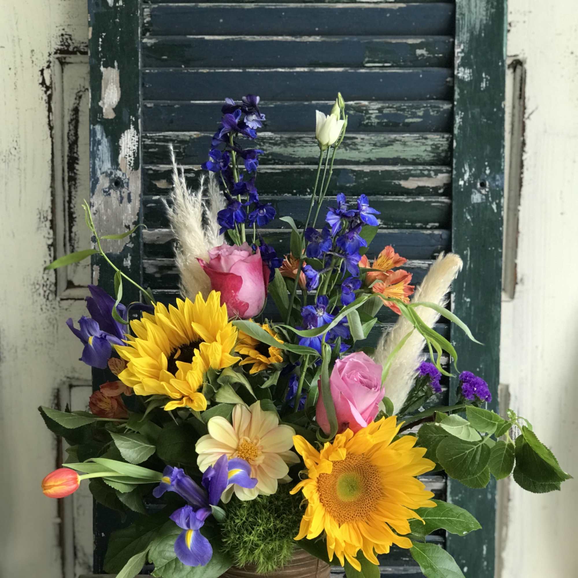 Mixed bouquet in a brown pot with sunflowers, pink roses, and purple blooms