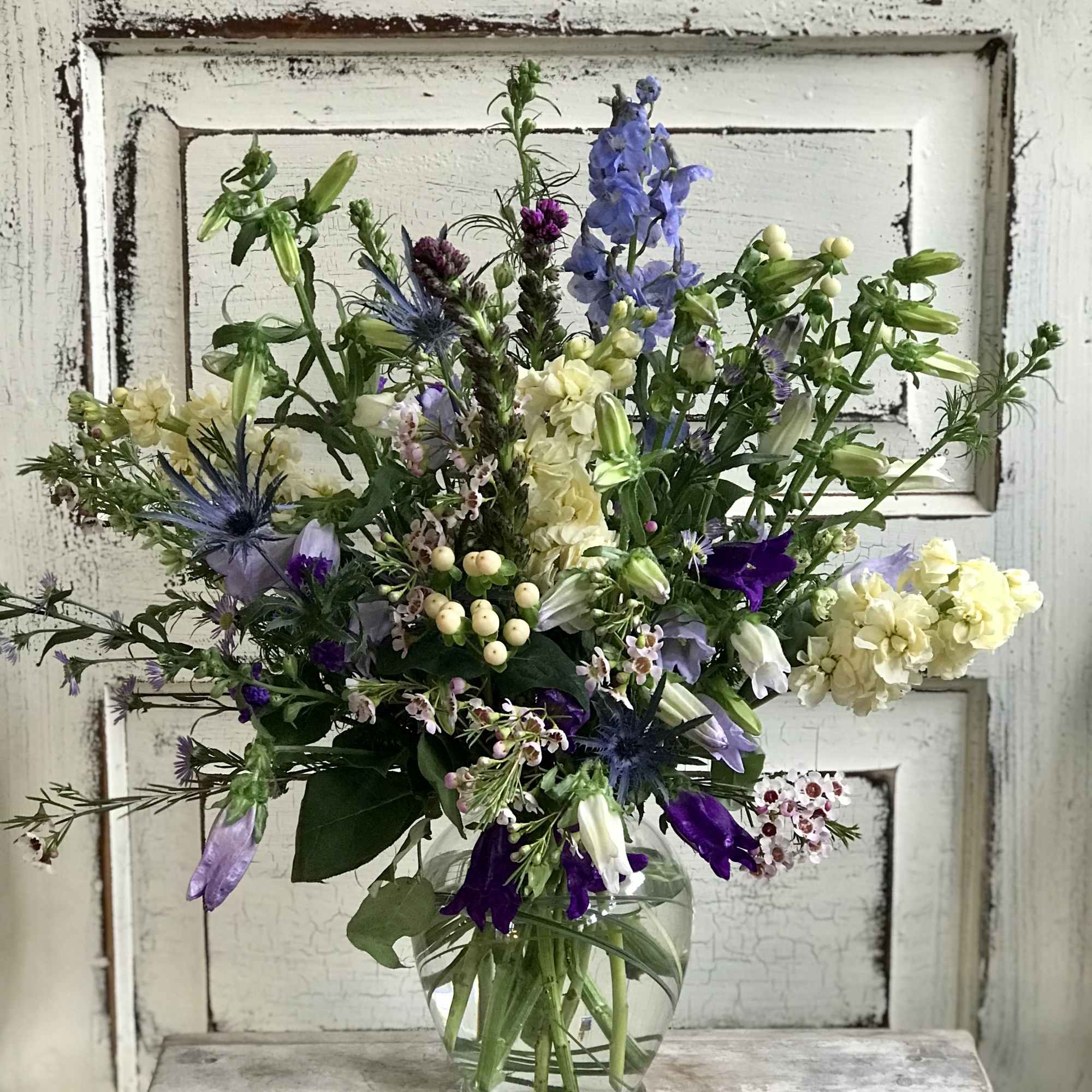 Mixed bouquet of purple, blue, and cream flowers in a clear glass vase