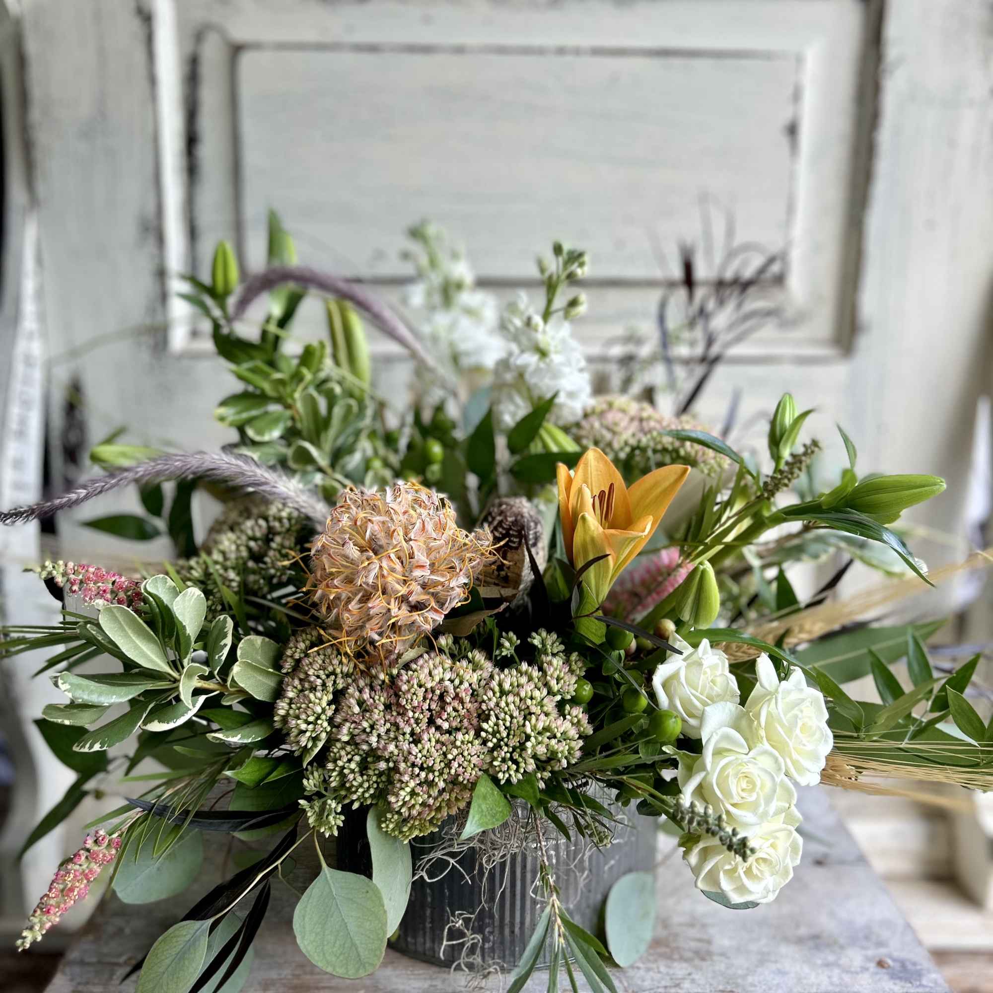 Mixed floral arrangement with white roses, orange lily, and greenery in a metal container