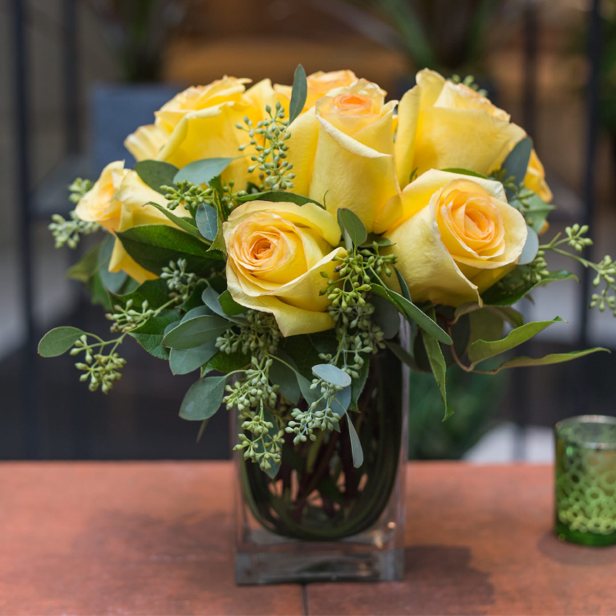 Yellow roses arranged in a clear square vase with greenery