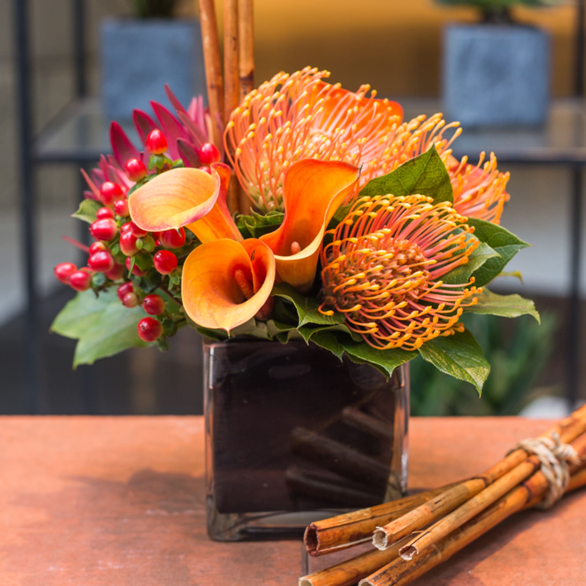 Orange calla lilies and pincushion protea in a square vase