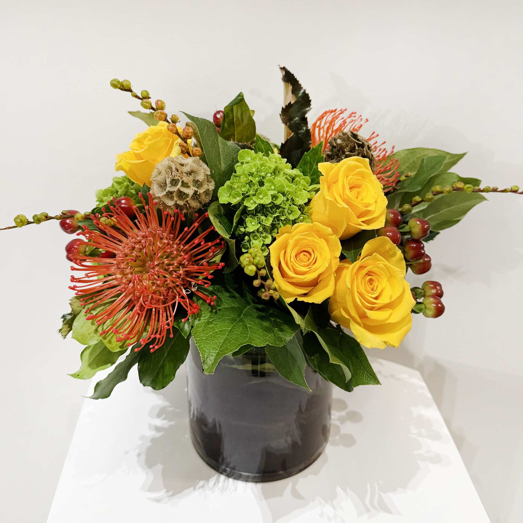 Yellow roses and red pincushion blooms in a black vase