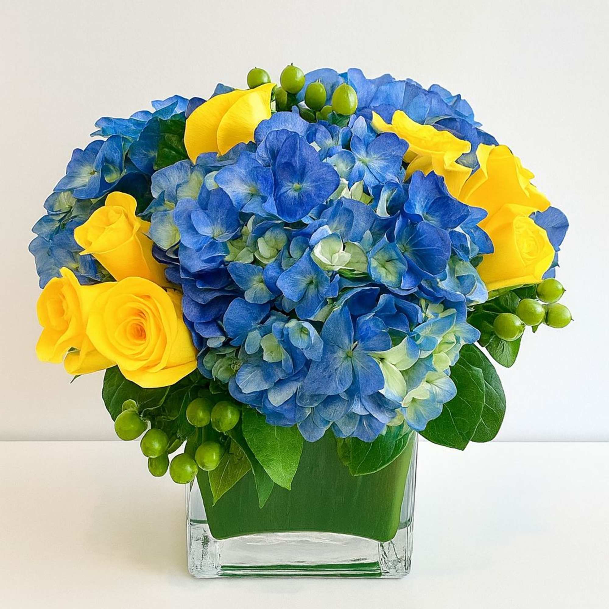 Blue hydrangeas and yellow roses in a clear square vase