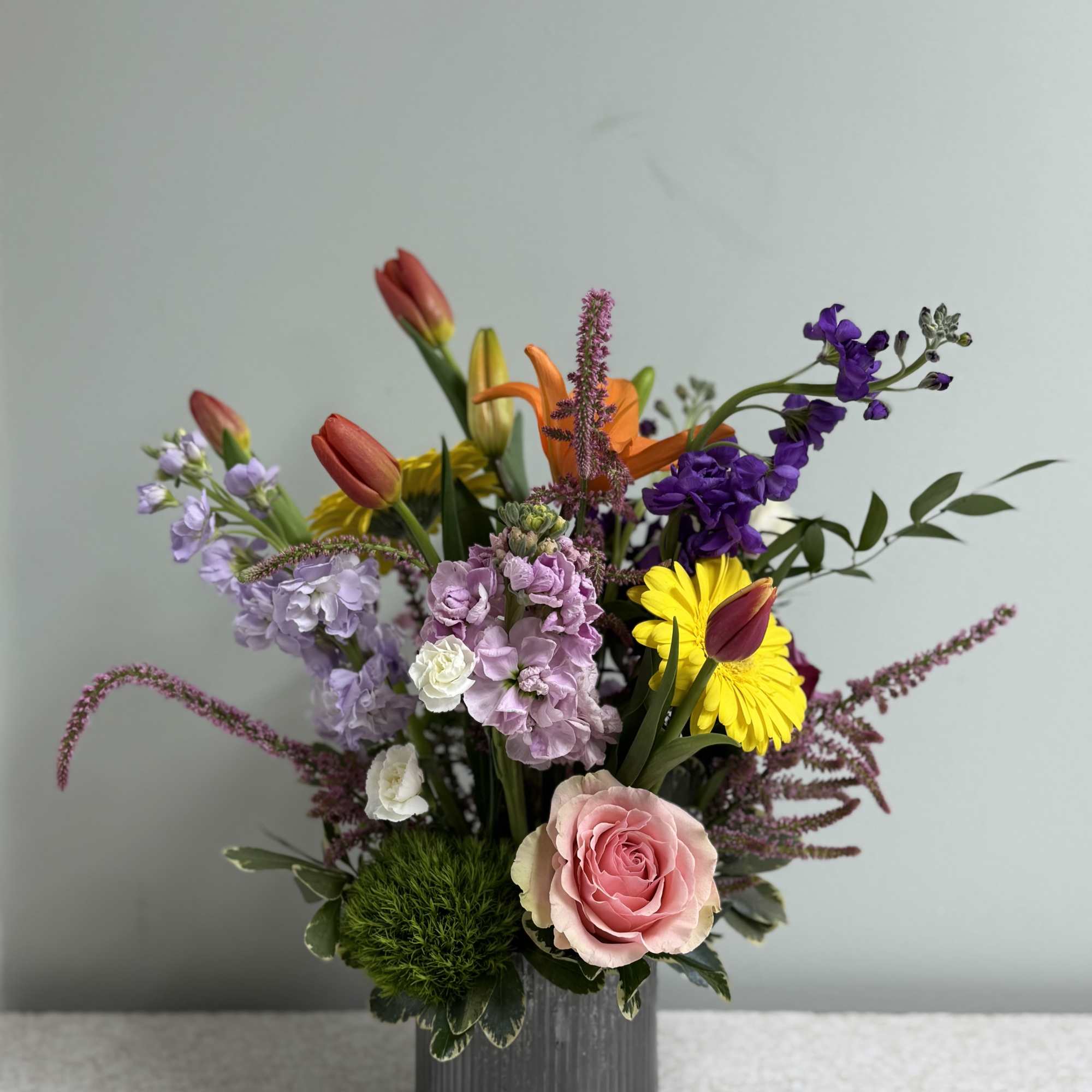 Mixed bouquet in a gray vase with pink rose, tulips, and purple flowers