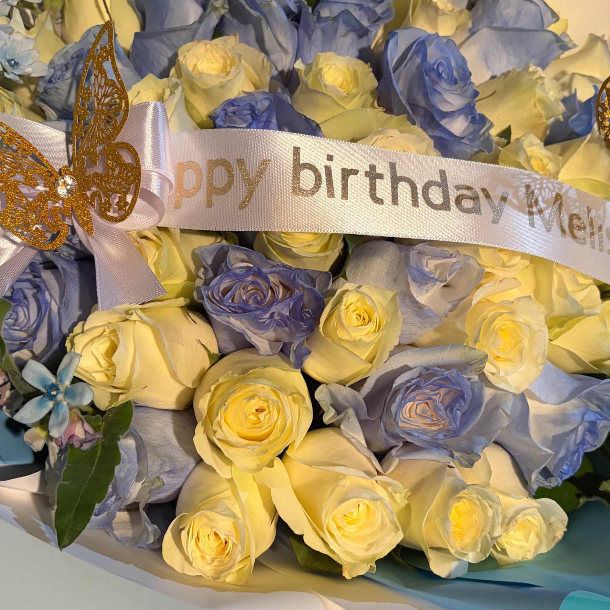 Bouquet of pale yellow and blue roses with a birthday ribbon