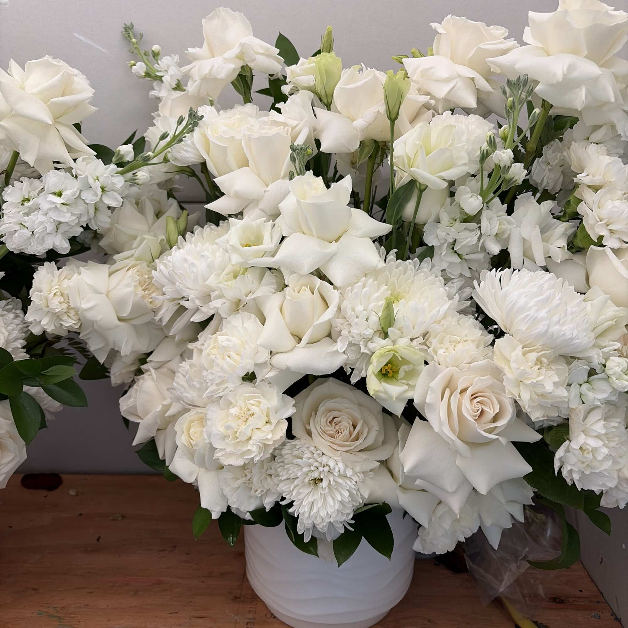 White floral arrangement in a white vase with roses, lilies, and mums