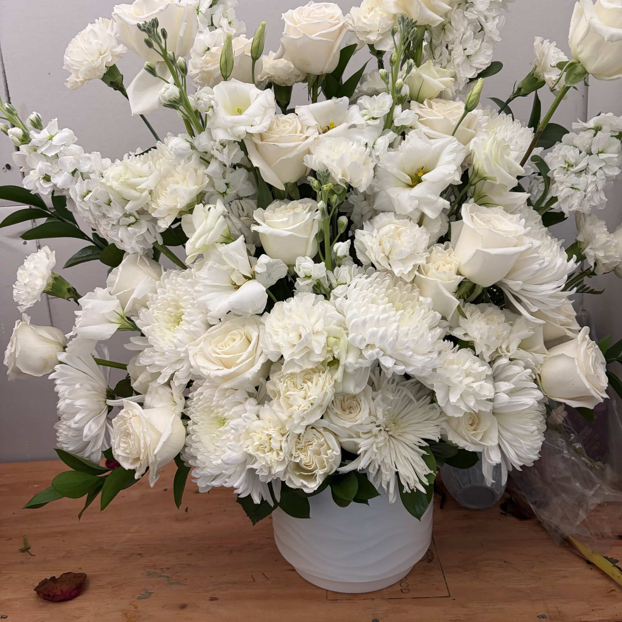 White floral arrangement in a white vase with roses and mixed blooms