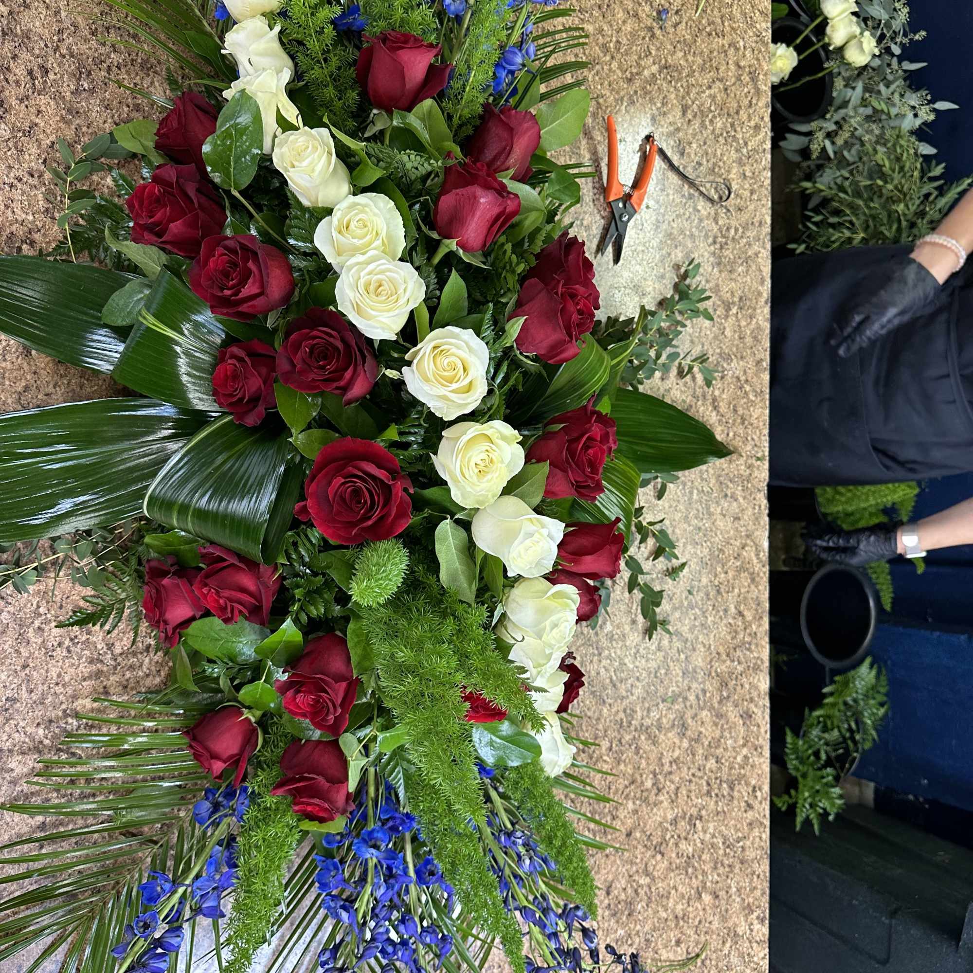 Red and white roses arranged with blue flowers and greenery.