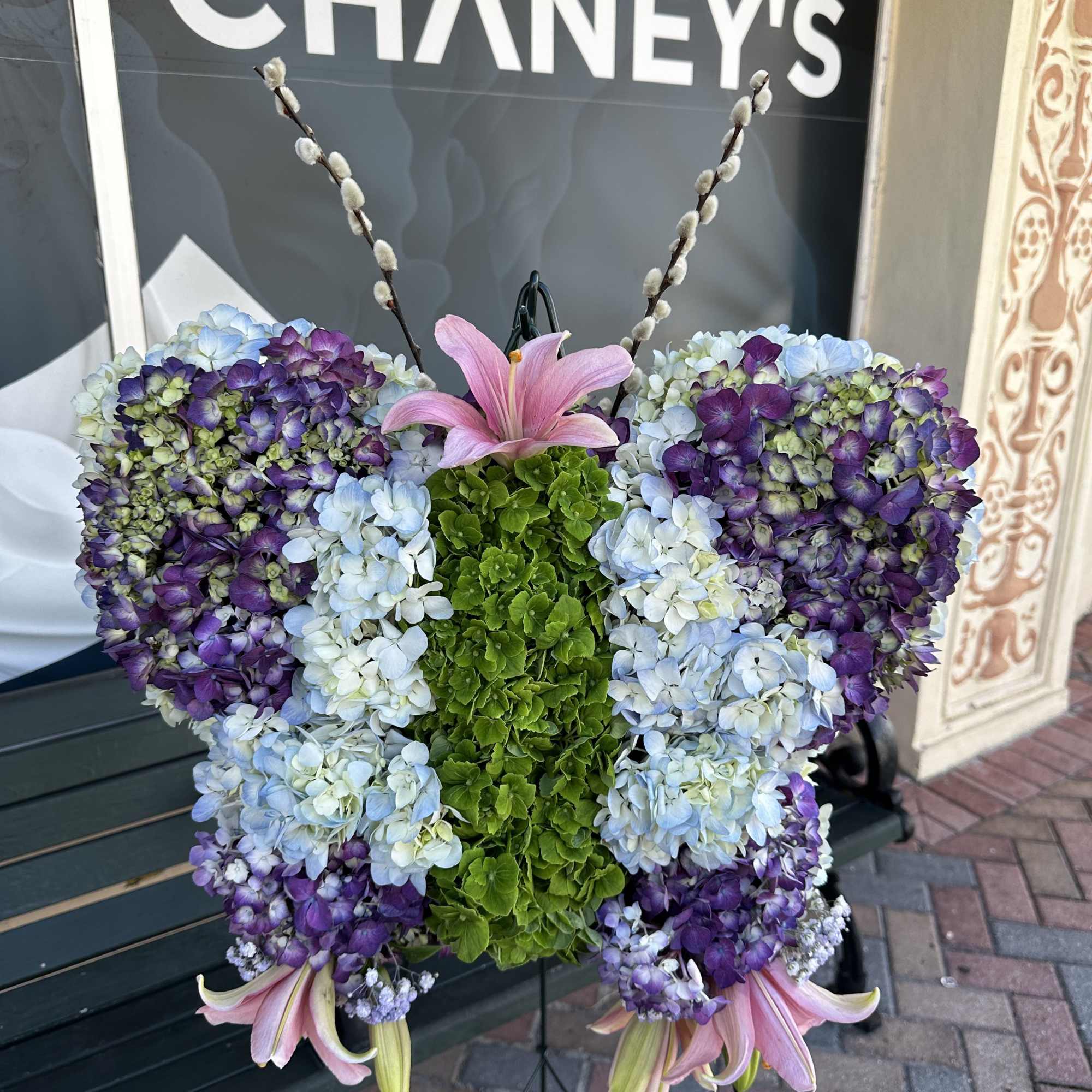 Butterfly-shaped floral arrangement with hydrangeas and pink lilies on an easel
