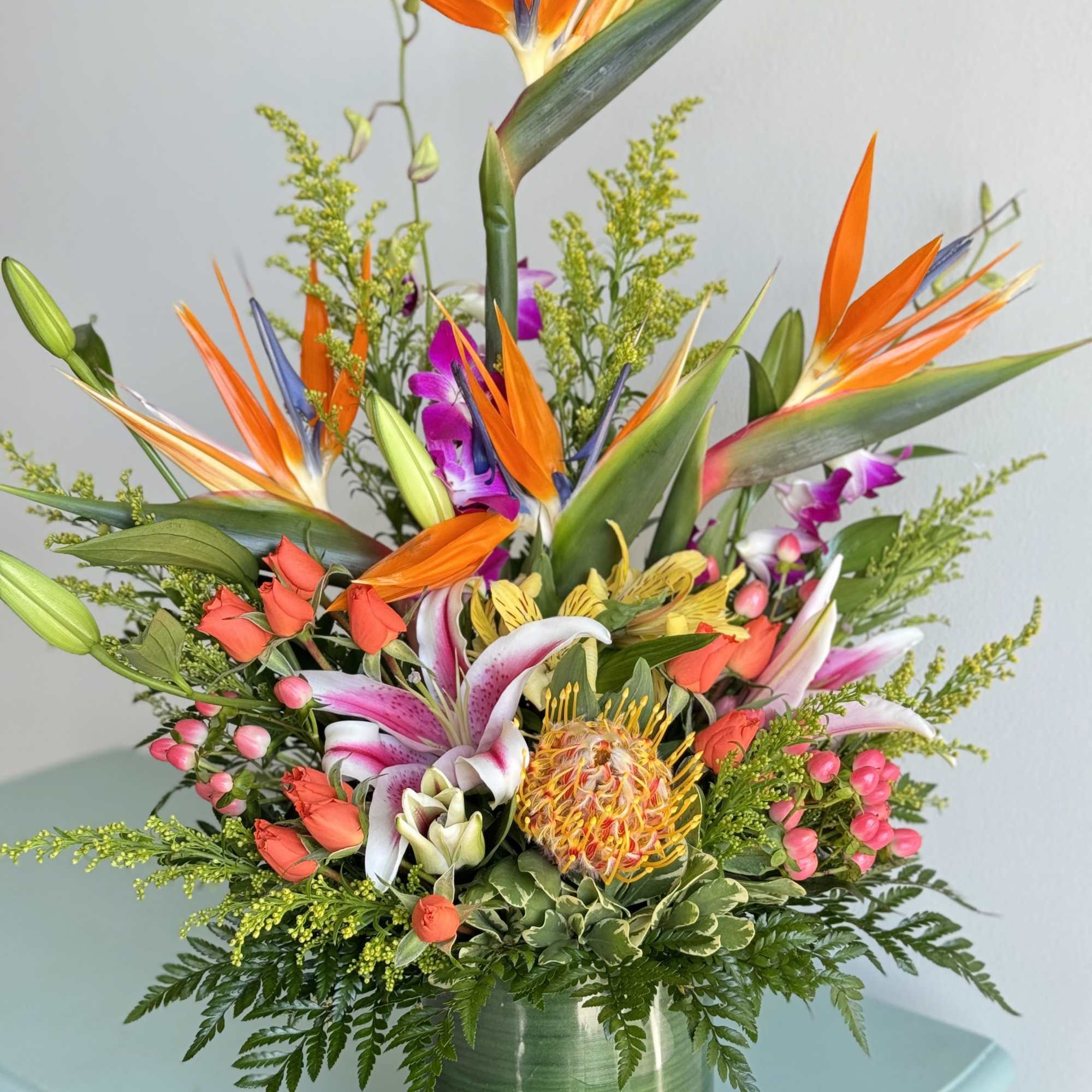 Tropical bouquet with bird of paradise, lilies, and orchids in a green vase