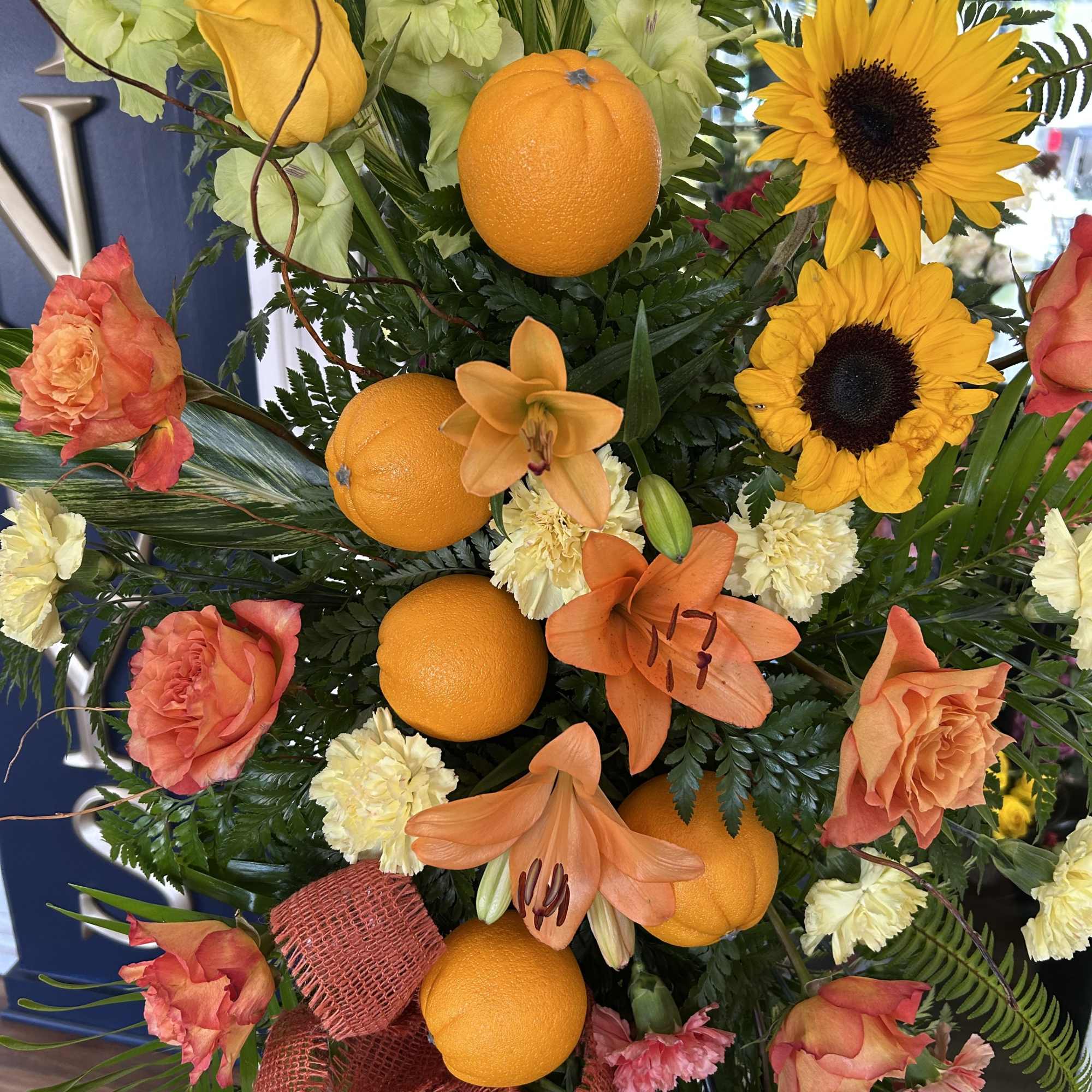 Orange and yellow floral arrangement with sunflowers, roses, lilies, and oranges