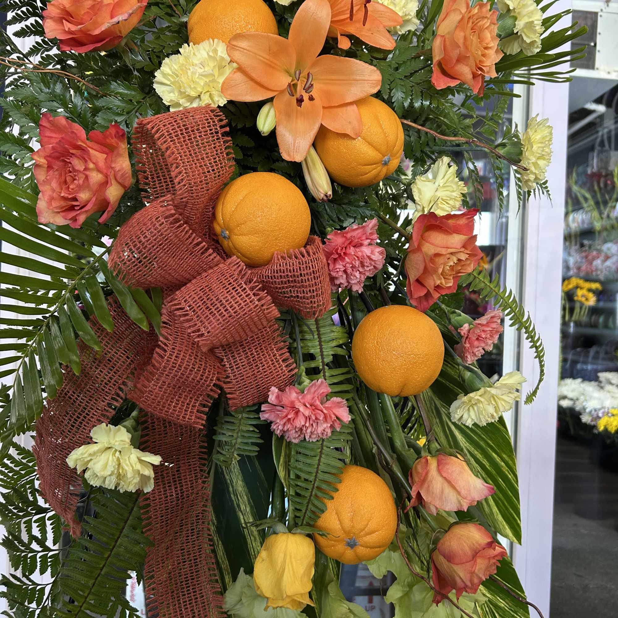 Orange and peach floral spray with oranges and a burgundy ribbon