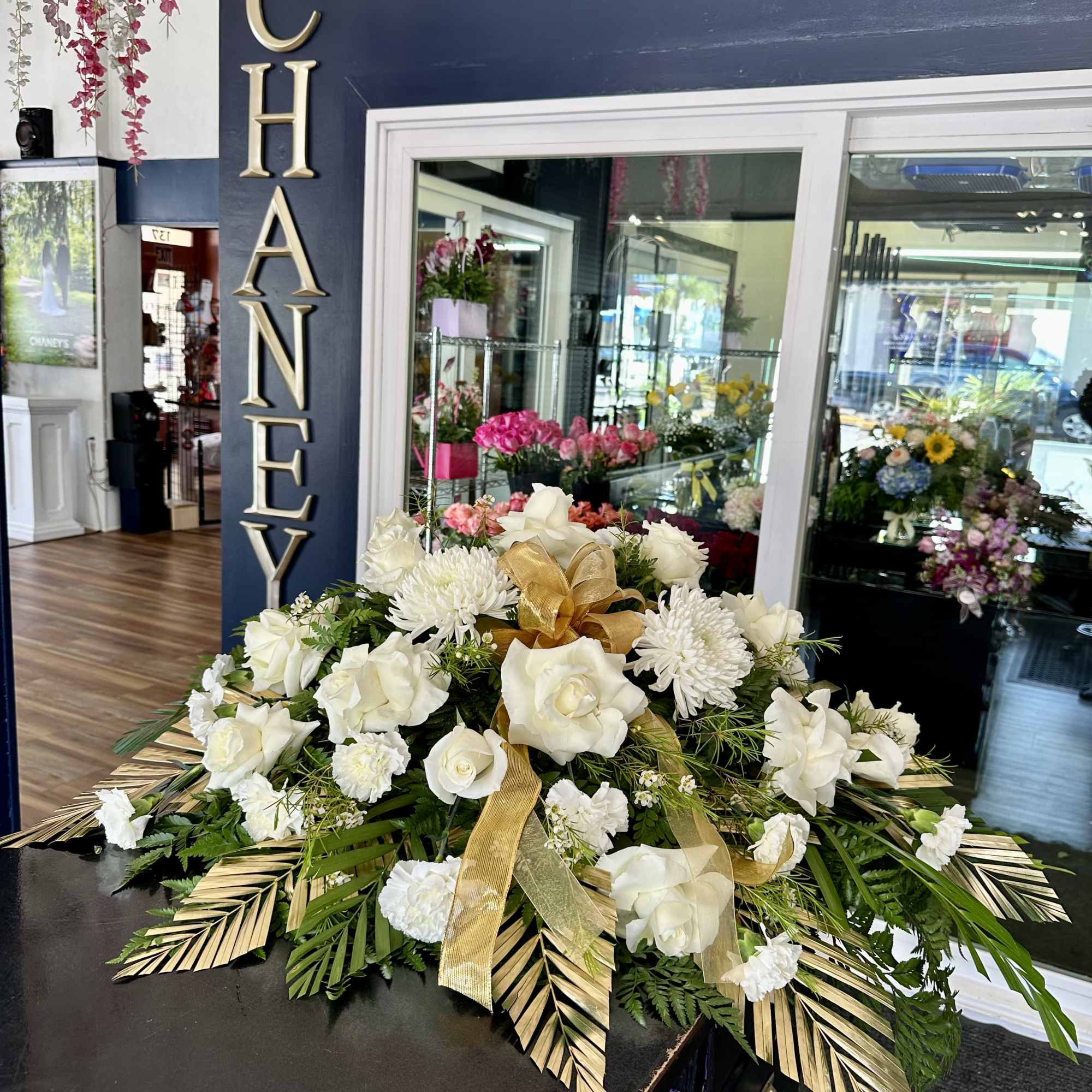 White floral arrangement with roses and chrysanthemums, accented by gold ribbon
