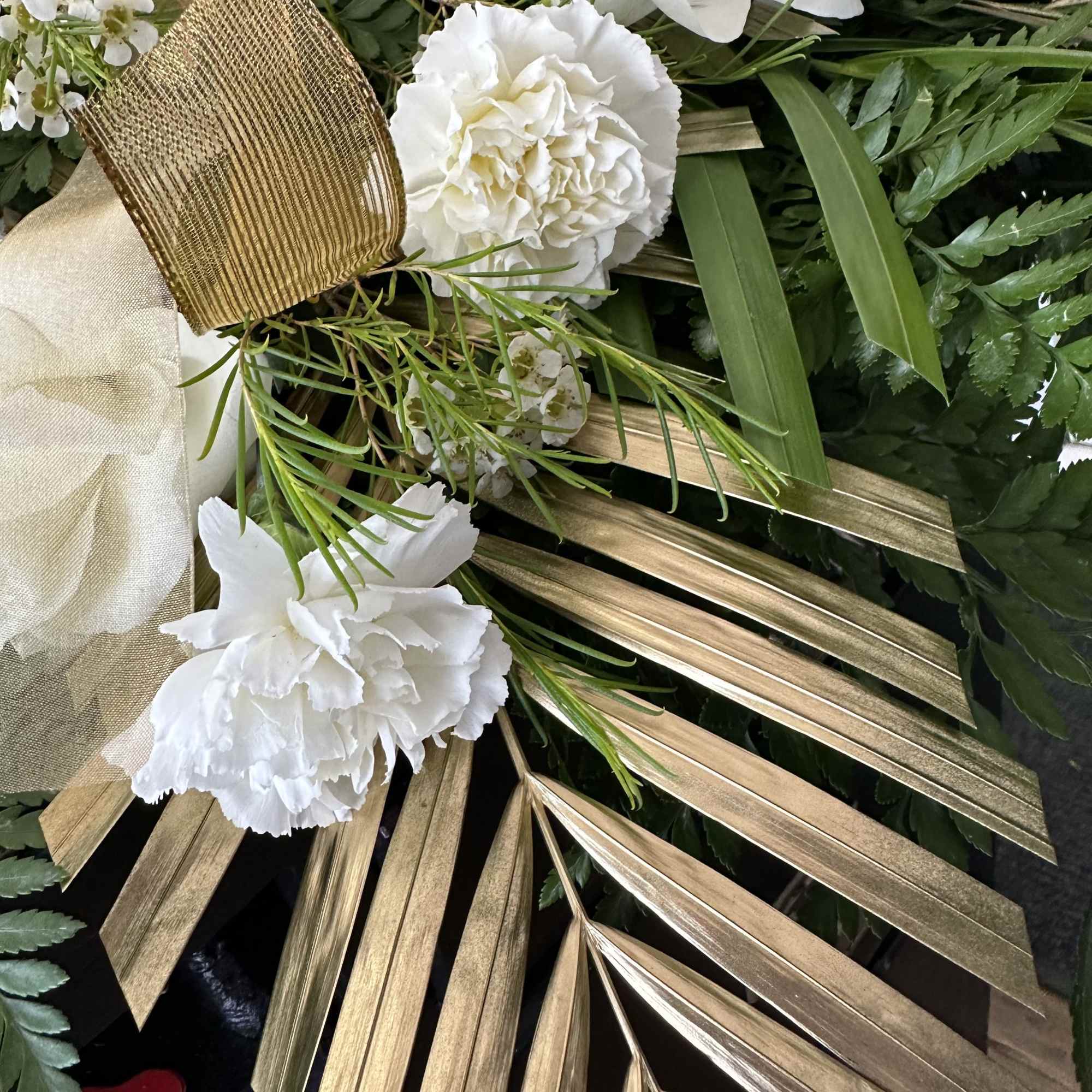 White carnations with gold palm fronds and ribbon accents