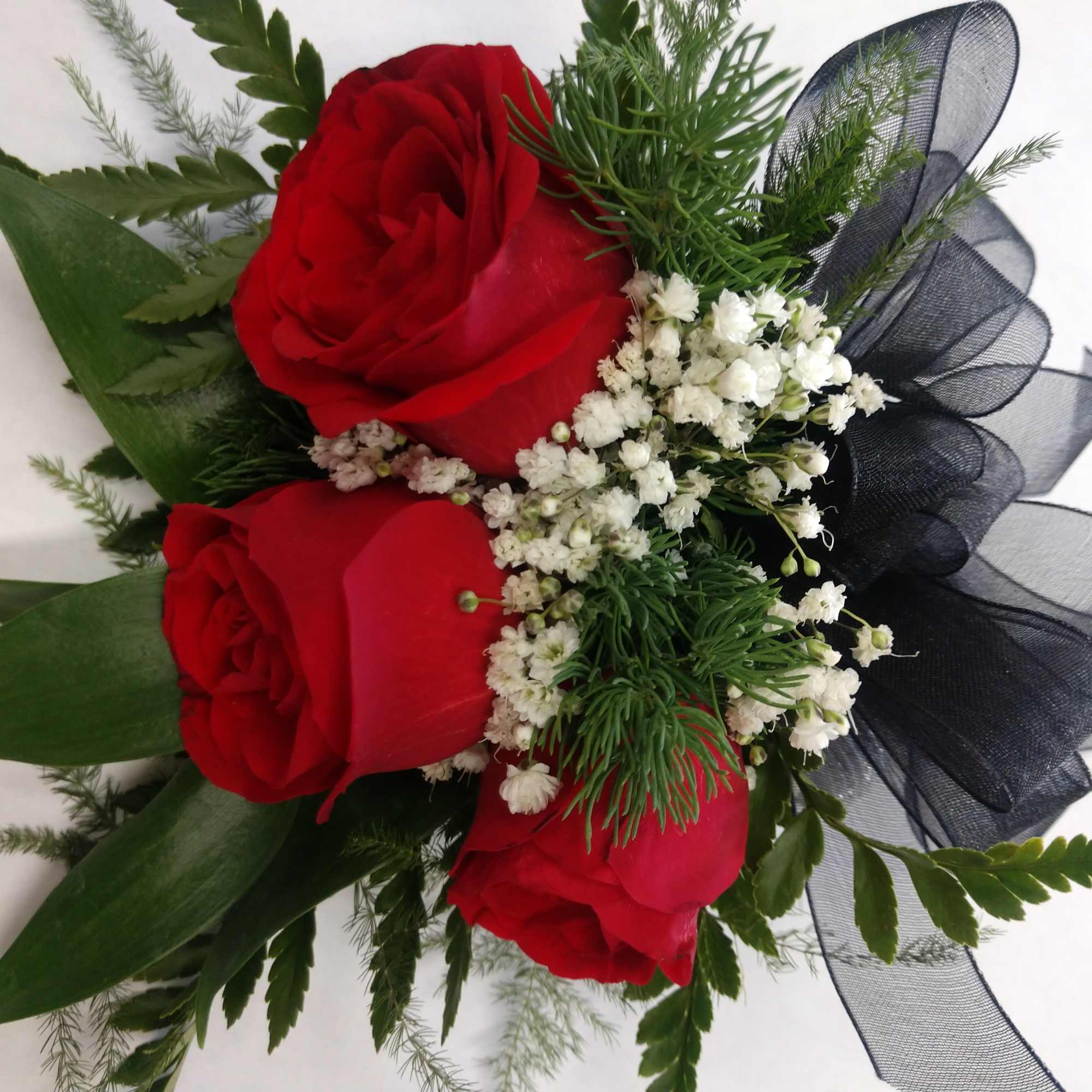 Three red roses with white filler and a black ribbon bow
