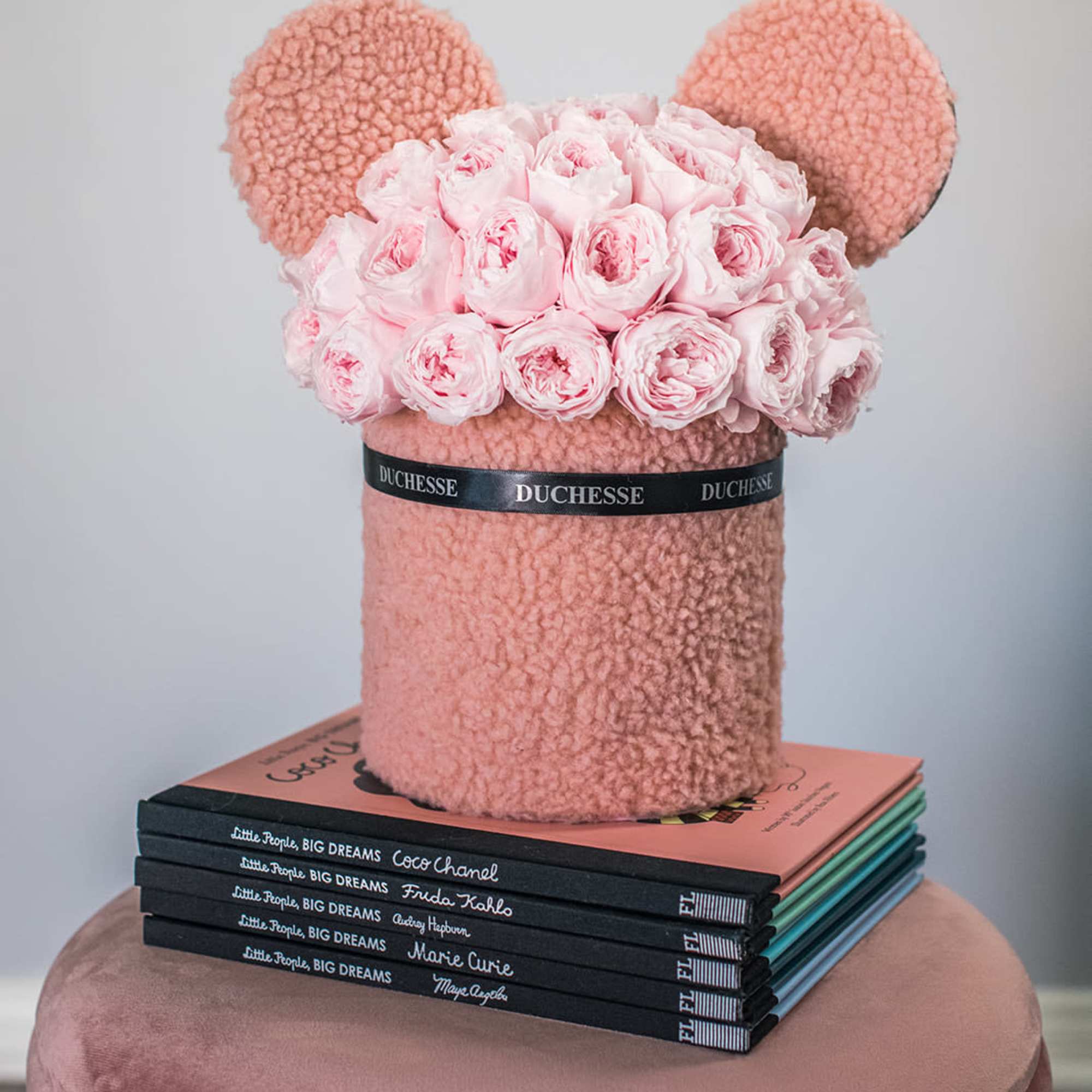 Pink rose arrangement in a plush teddy bear-shaped box on stacked books