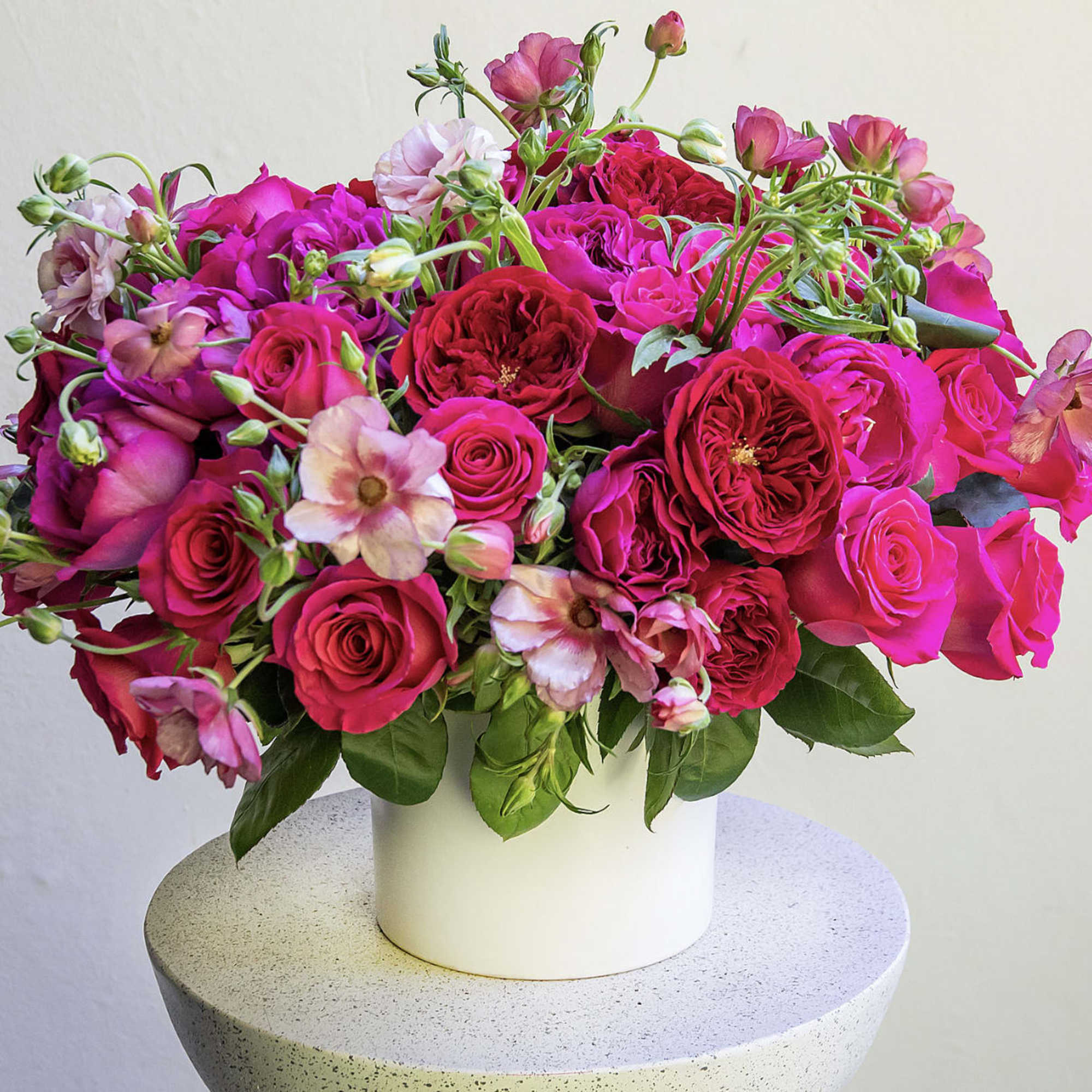 Bright pink and red roses with small pink flowers in a white vase